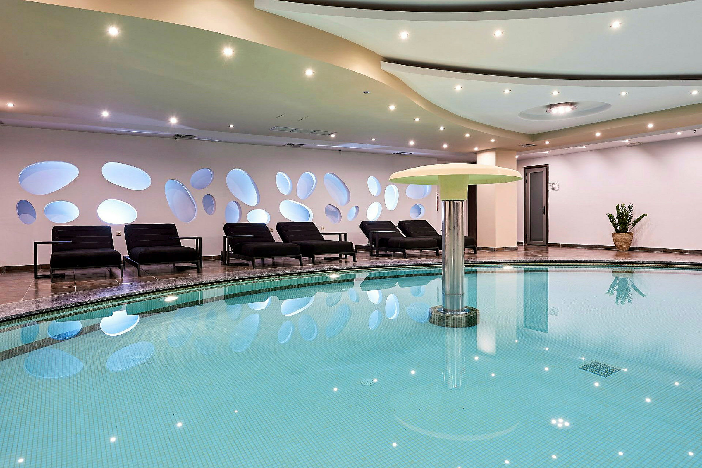 Interiør af et spa med en swimmingpool og solsenge. (AI-genereret tekst)