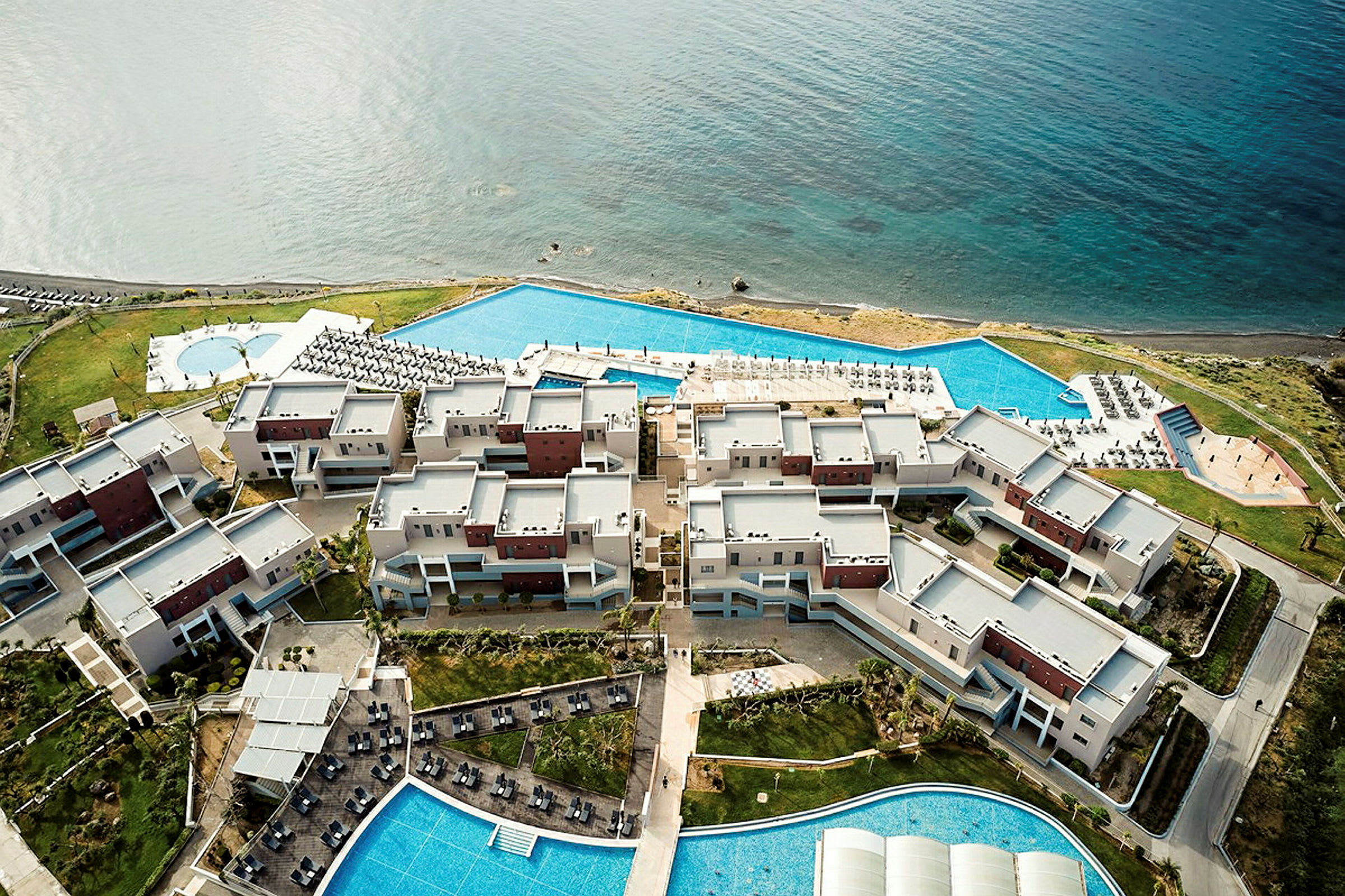 Luftfoto af et hotelkompleks ved havet med swimmingpools og udendørs områder. (AI-genereret tekst)