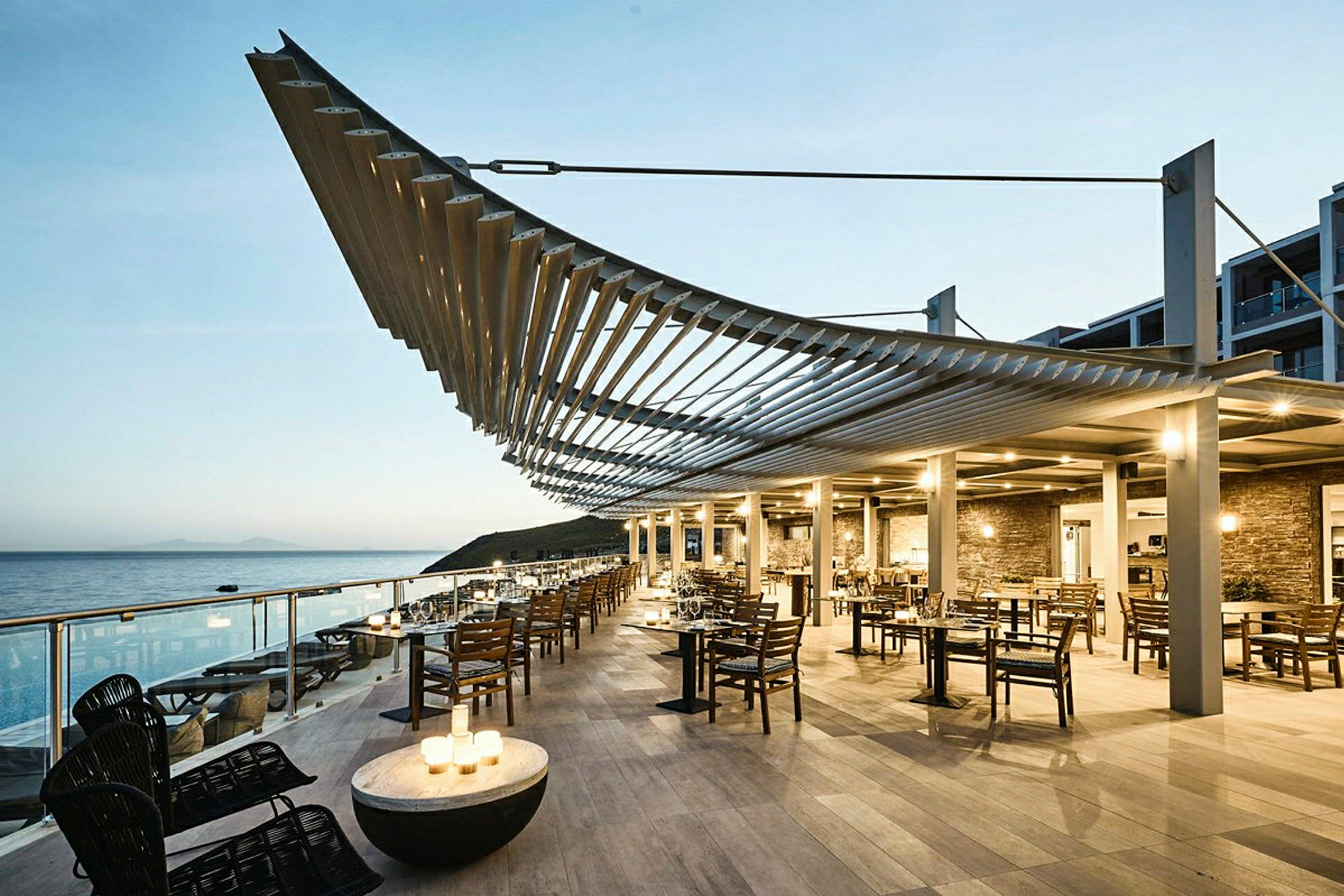 Restaurant med siddepladser udendørs ved havet under en moderne pergola. (AI-genereret tekst)