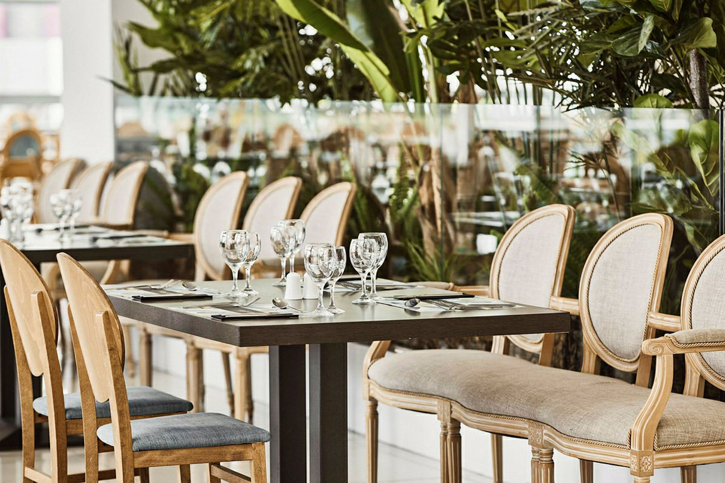 En række spiseborde og stole i en restaurant omgivet af grønt. (AI-genereret tekst)