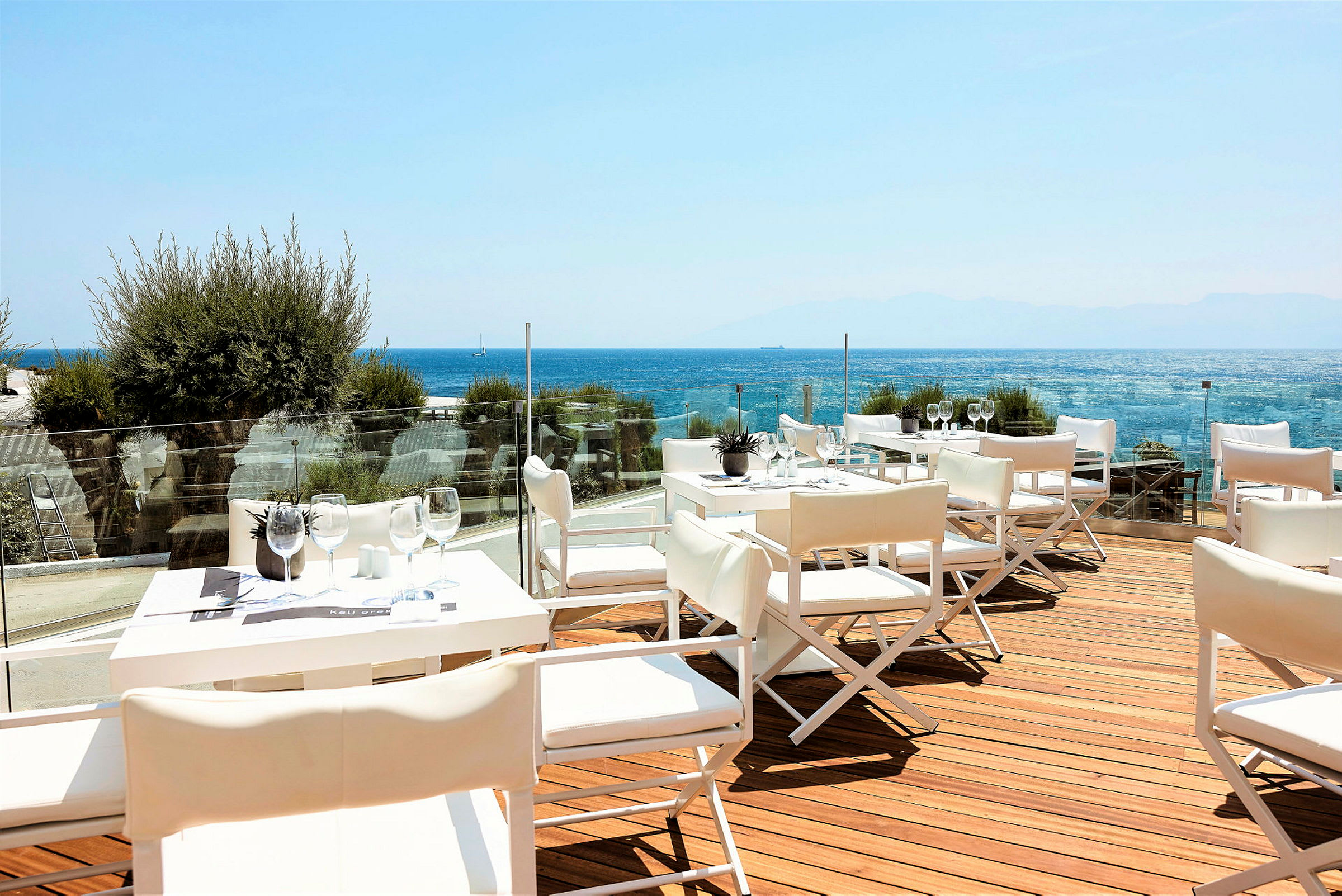 En terrasse med hvide borde og stole, udsigt over havet. (AI-genereret tekst)