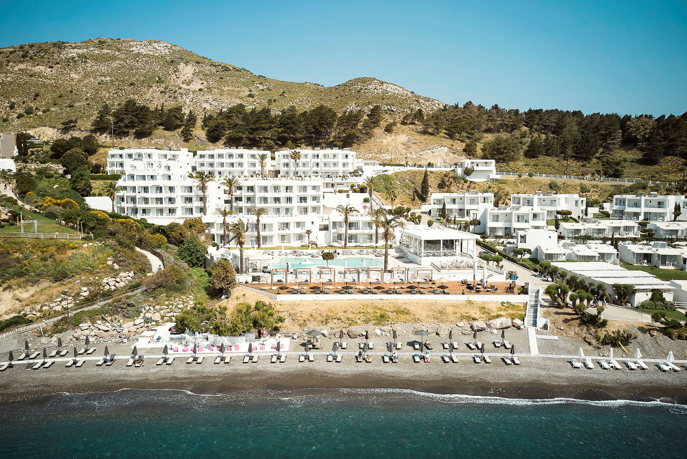 Hotelkompleks ved stranden med poolområde og omkringliggende grønne områder. (AI-genereret tekst)