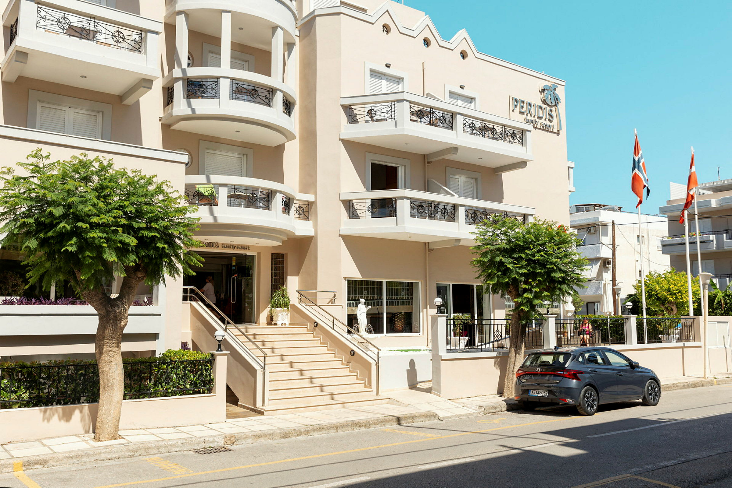 Hotellets facade med indgang, altaner og en parkeret bil udenfor. (AI-genereret tekst)