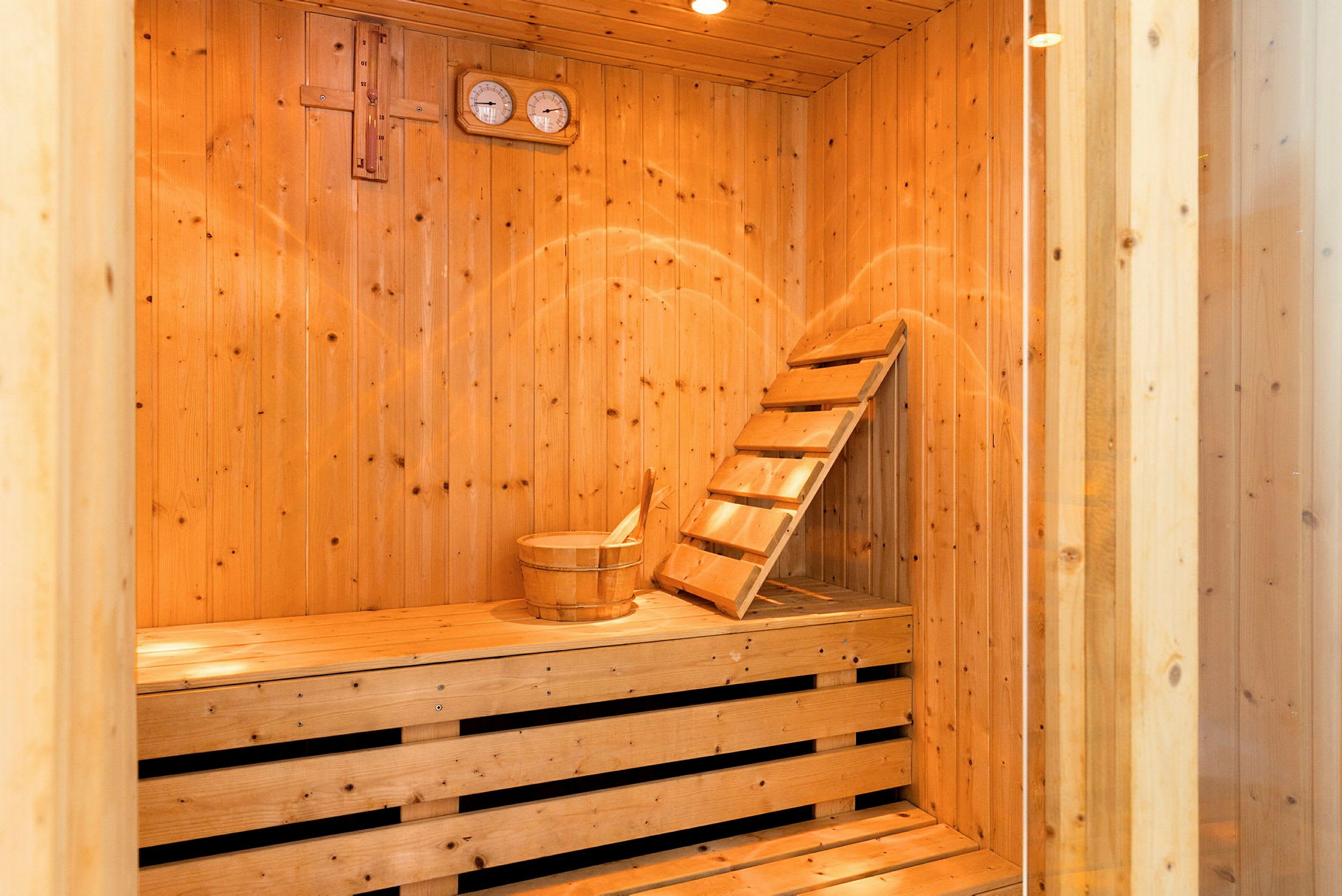 Interiør i en sauna med træpaneler, en bænk og en spand. (AI-genereret tekst)