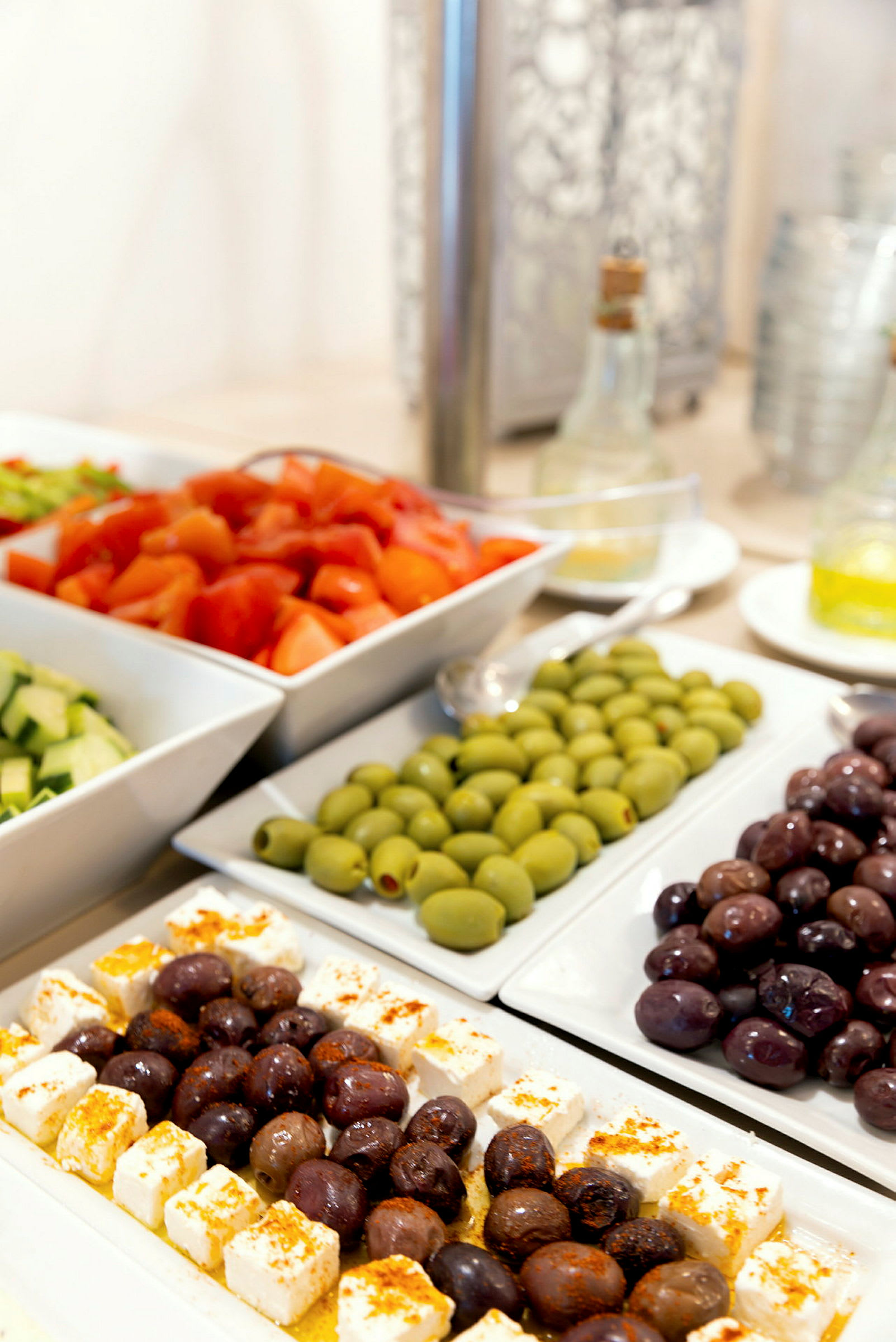 Flere serveringsfade med salatingredienser som oliven, fetaost og tomater. (AI-genereret tekst)