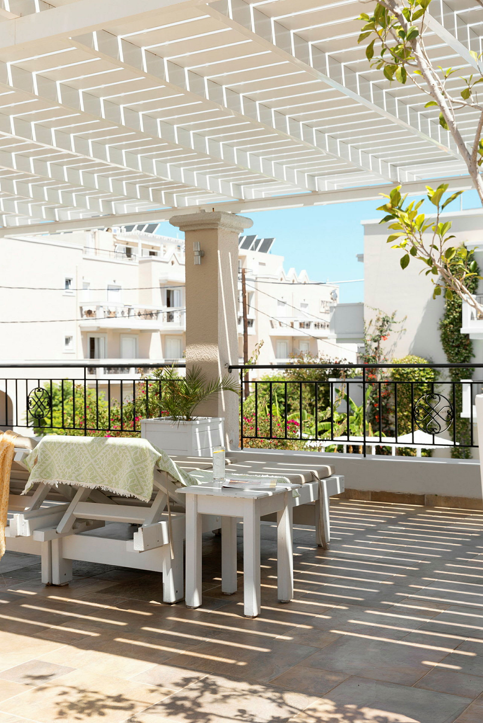 Udendørsområde med hvid pergola, havemøbler og udsigt til bygninger og grønne områder. (AI-genereret tekst)