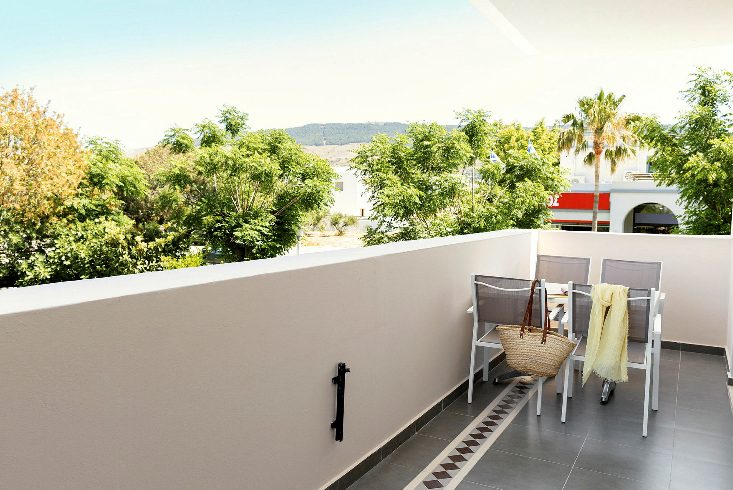 En balkon med bord, stole og udsigt til træer og bygninger. (AI-genereret tekst)