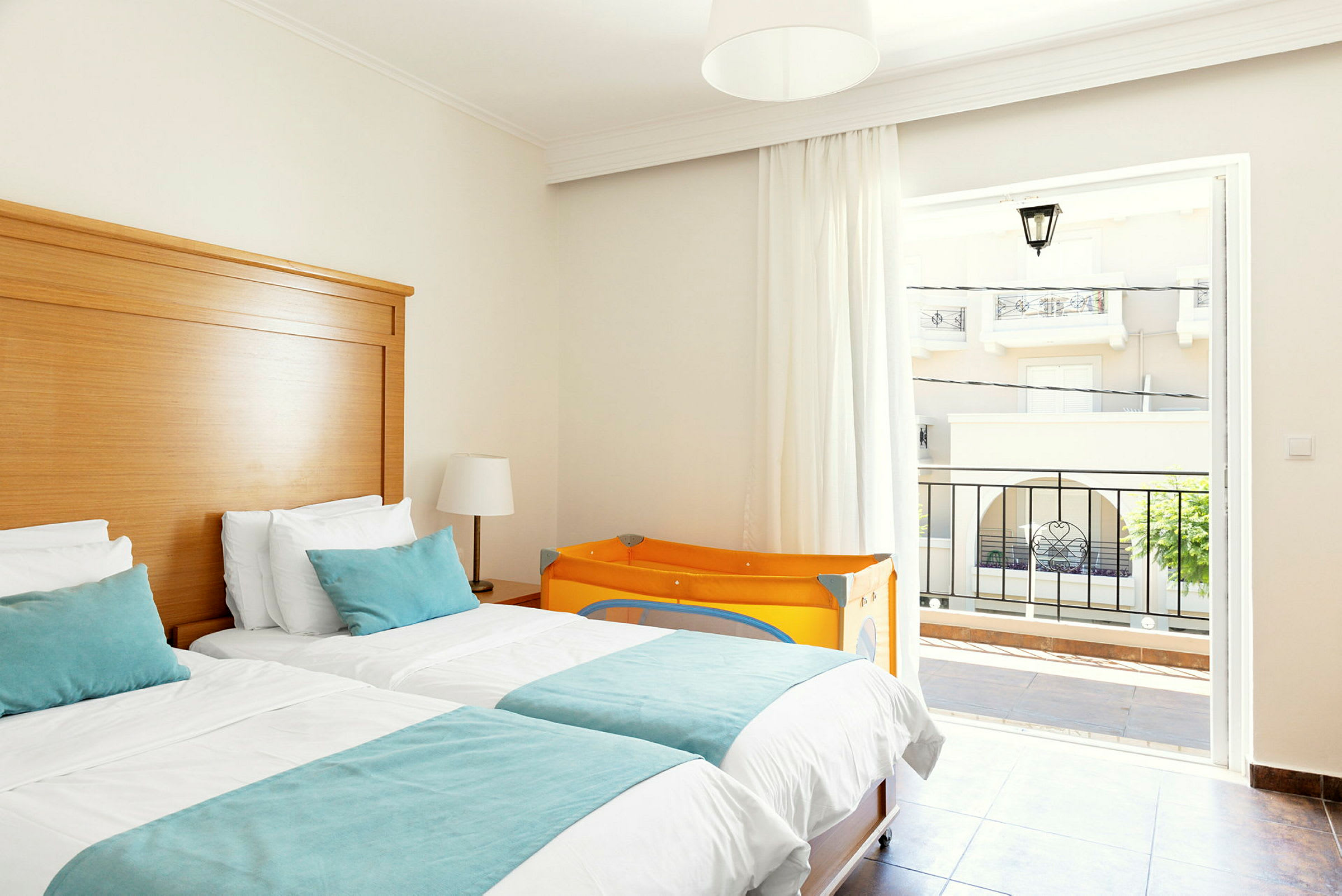 Hotelværelse med to enkeltsenge, lyse møbler og en orange barneseng. (AI-genereret tekst)