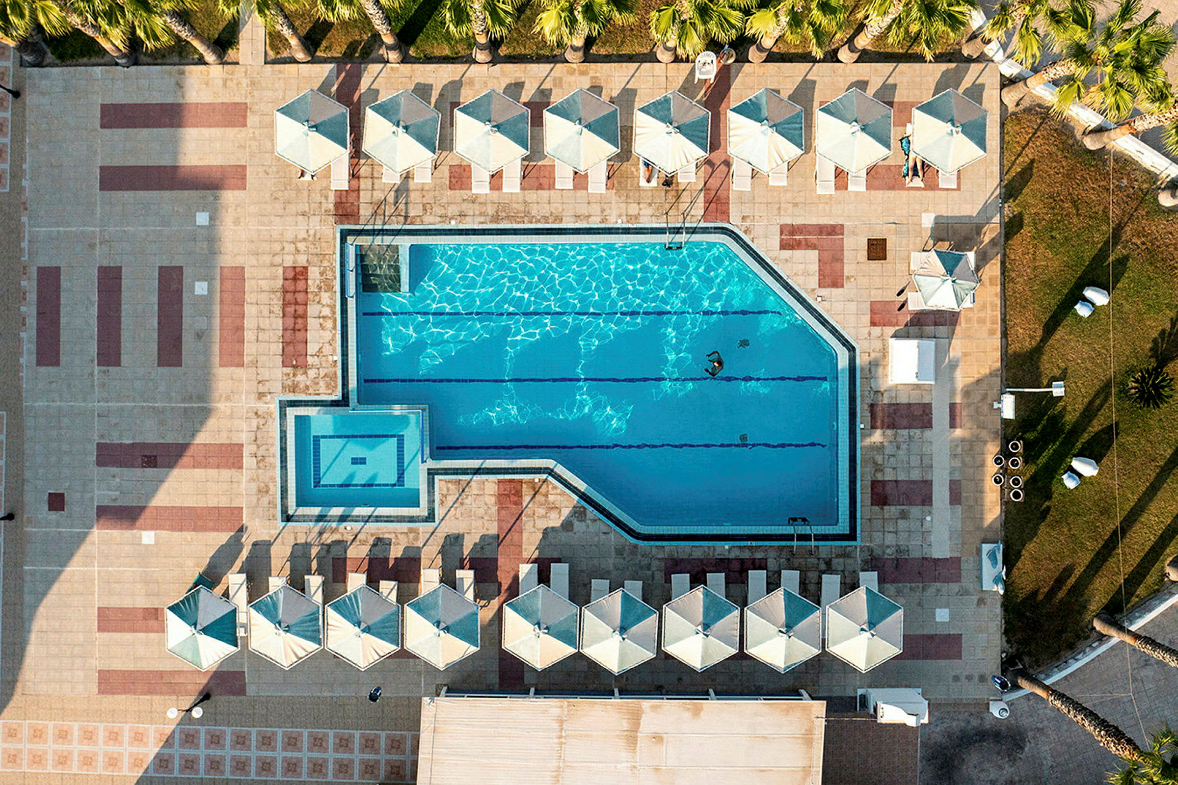 Et overblik over en pool med parasoller og liggestole rundt omkring. (AI-genereret tekst)