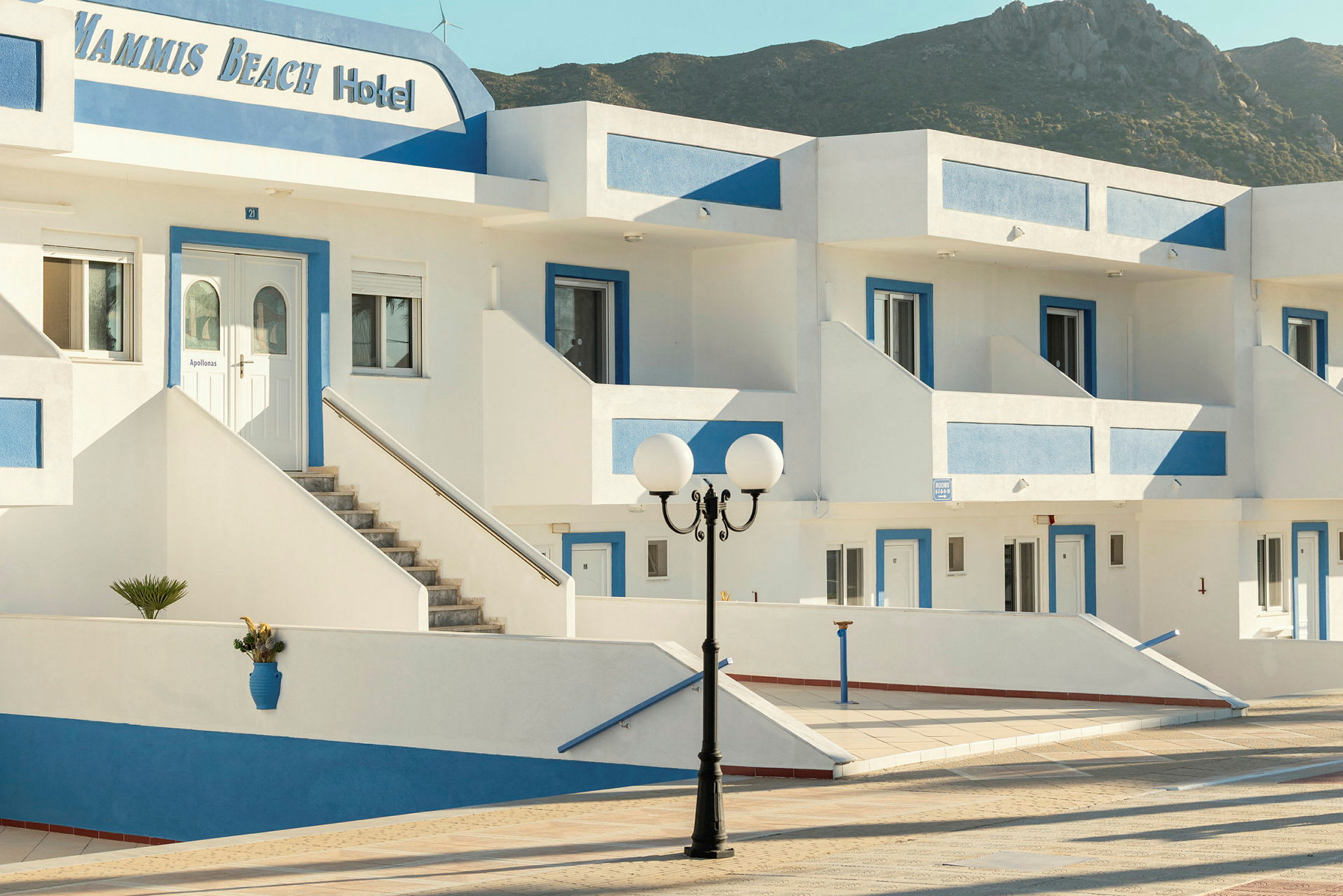 Billede af hotelbygning med hvid facade og blå detaljer. (AI-genereret tekst)