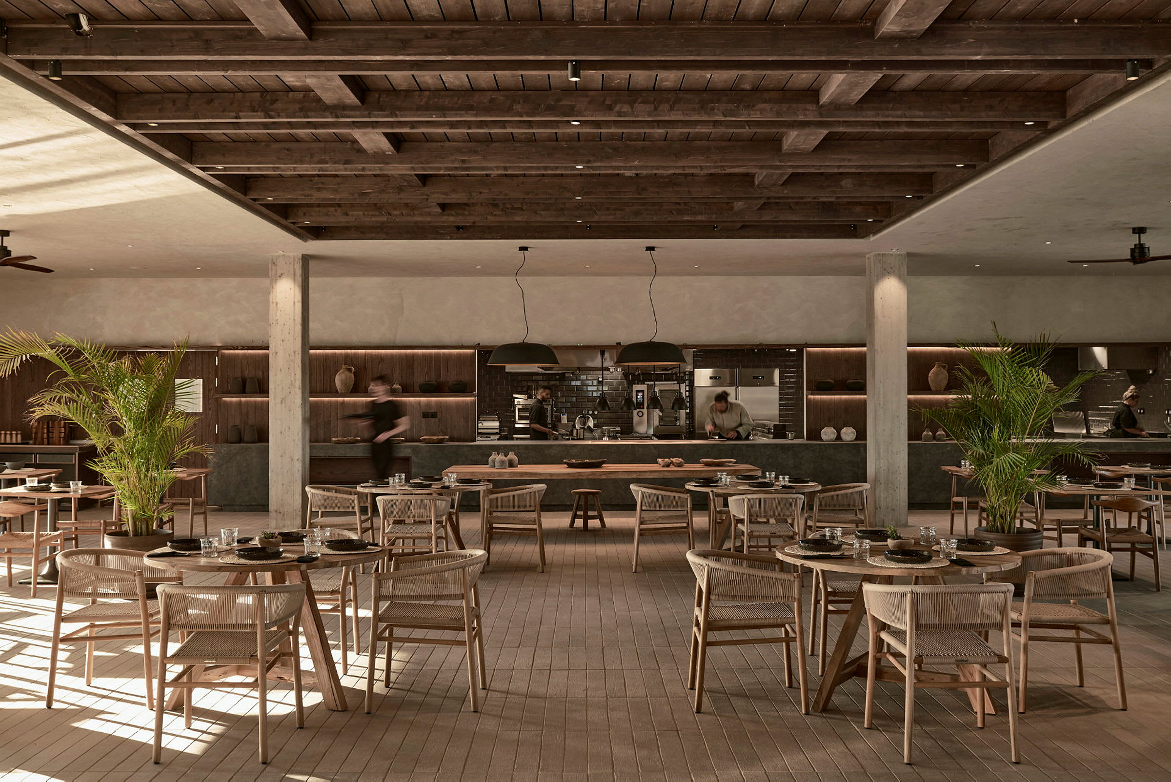 Restaurant med træindretning og borde spredt over gulvet, med åbent køkkenområde i baggrunden. (AI-genereret tekst)