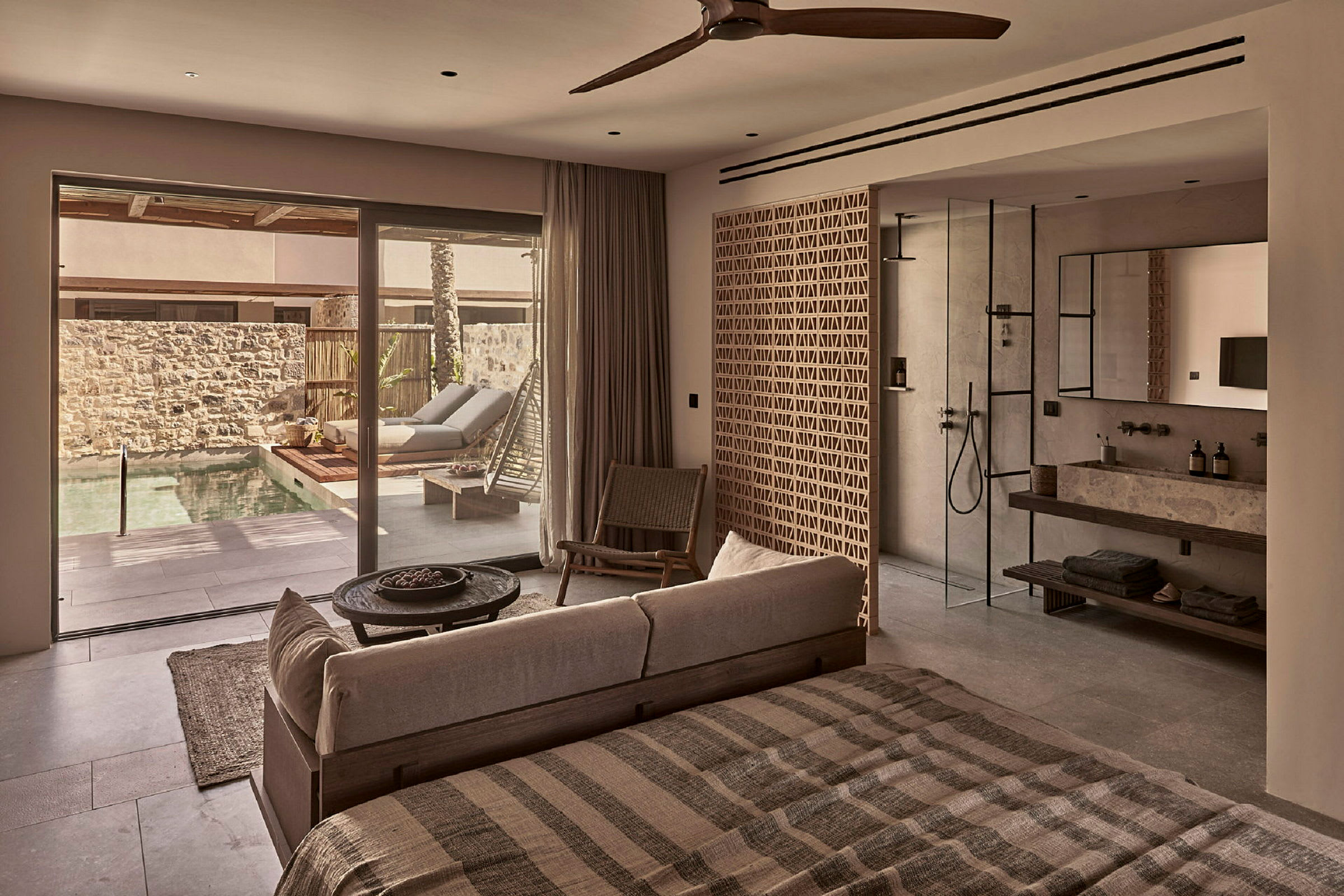 Interiør af et moderne hotelværelse med seng, siddeområde og badeværelse, udsigt til en privat pool gennem glasdøre. (AI-genereret tekst)
