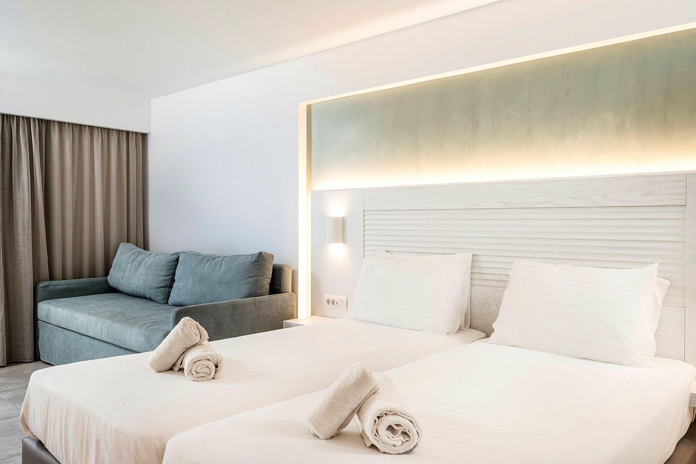 Hotelværelse med to enkeltsenge, oplyst sengegavl og en sofa. (AI-genereret tekst)