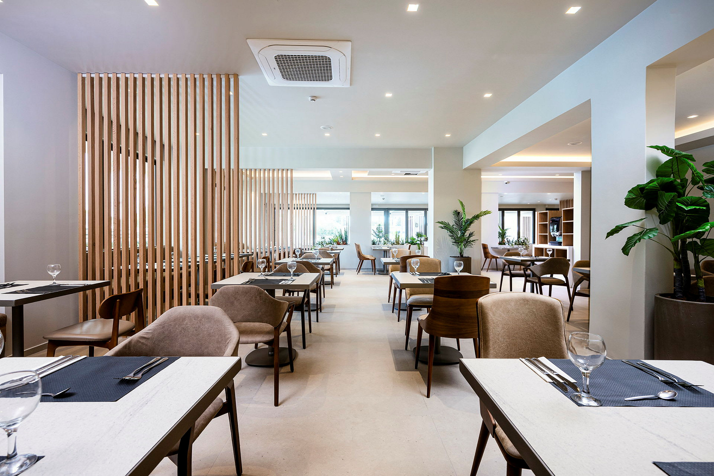 En moderne restaurant med borde og stole samt grønne planter. (AI-genereret tekst)
