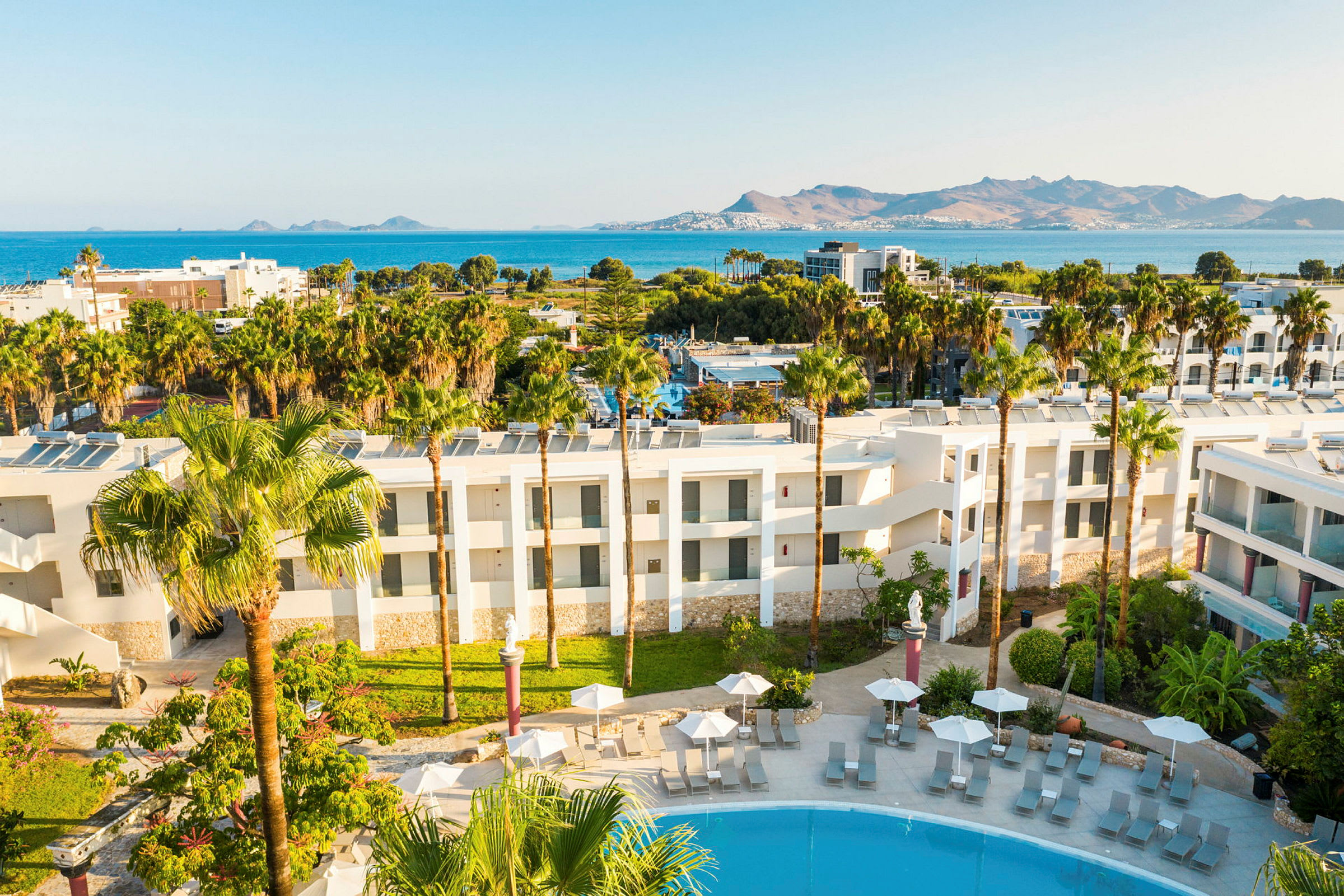 Hotellets ydre med poolområde og udsigt over havet og bjergene. (AI-genereret tekst)