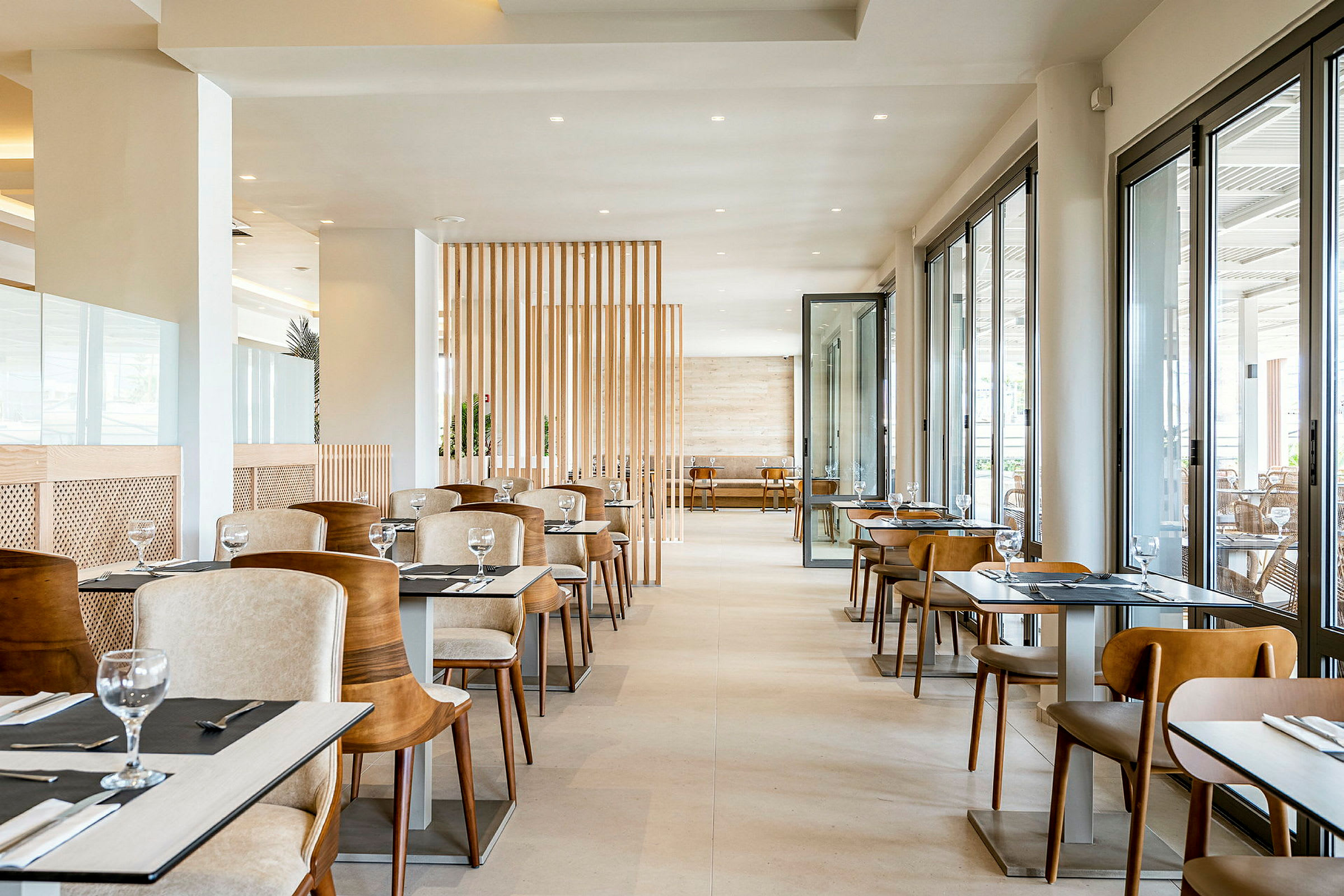 Restaurantinteriør med borde og stole. Området er lyst og moderne med store vinduer, der lukker dagslys ind. (AI-genereret tekst)