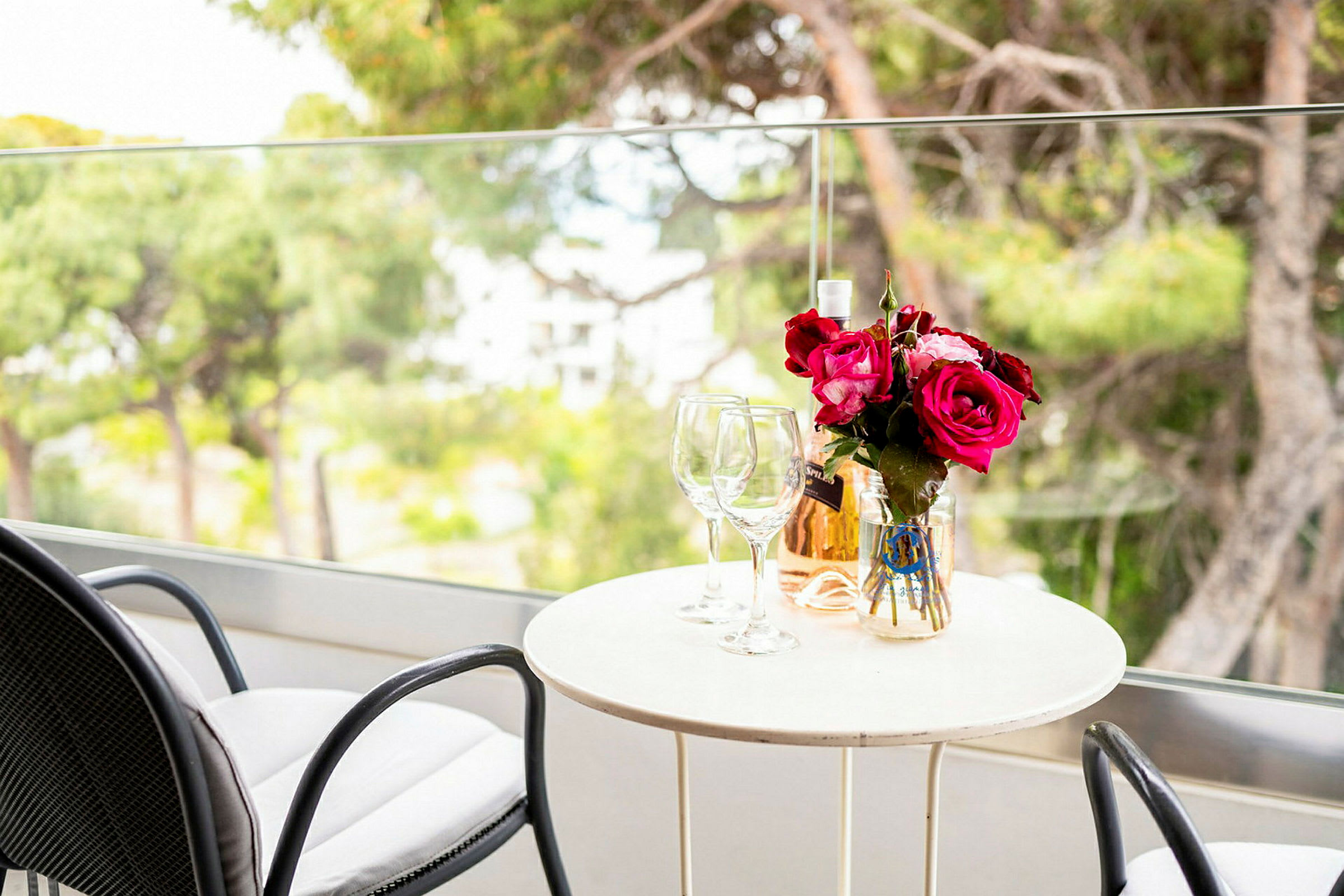 Et bord med to glas, en vase med rosa blomster og en flaske rosévin på en altan. (AI-genereret tekst)