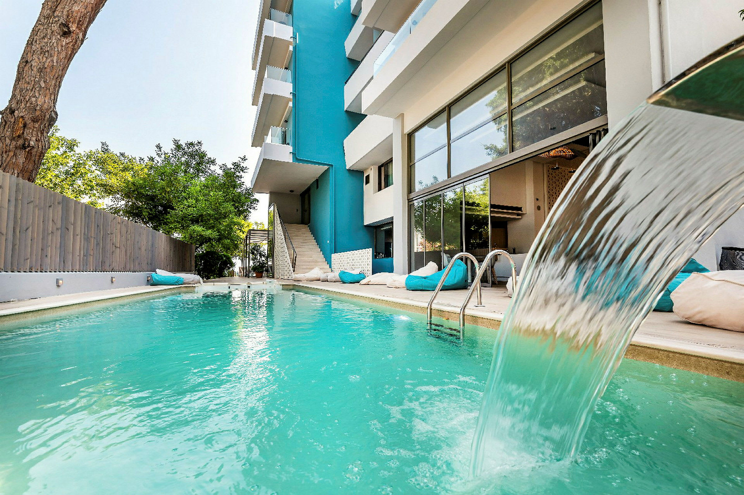 Udendørs swimmingpool med vandfald ved siden af en moderne bygning. (AI-genereret tekst)