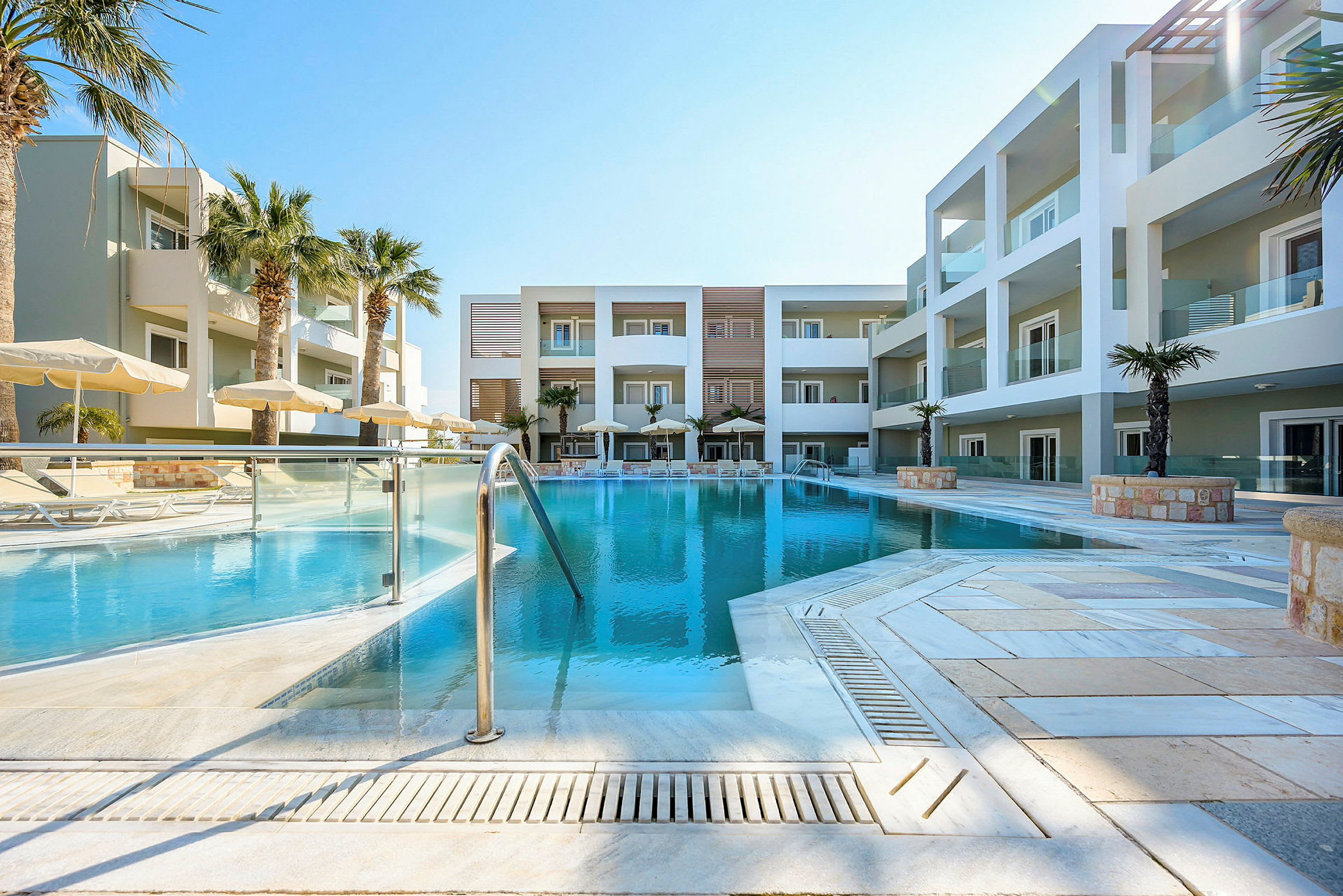 En pool foran et moderne hotel med palmer og parasoller. (AI-genereret tekst)