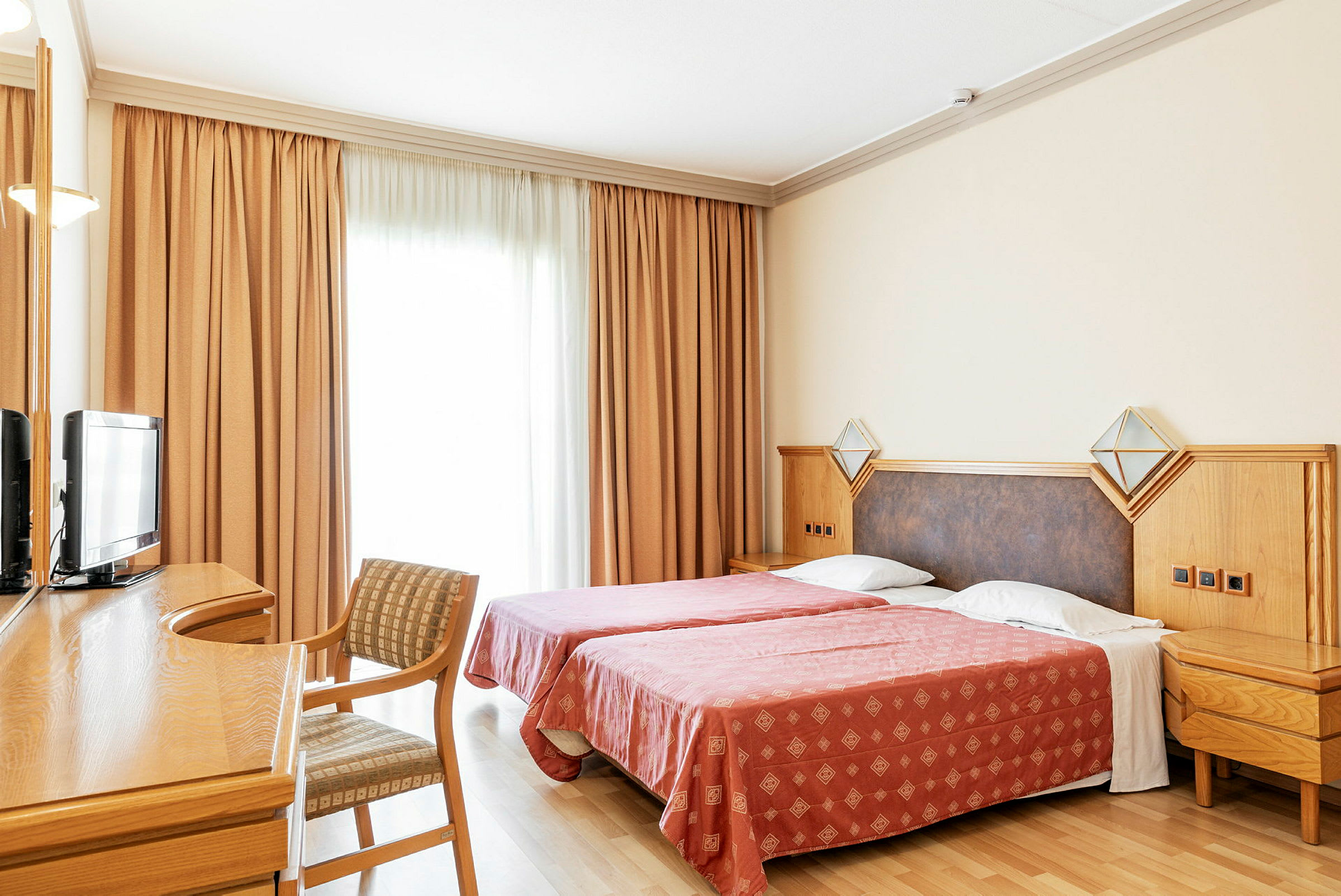Hotelværelse med to enkeltsenge, skrivebord, stol og tv. (AI-genereret tekst)