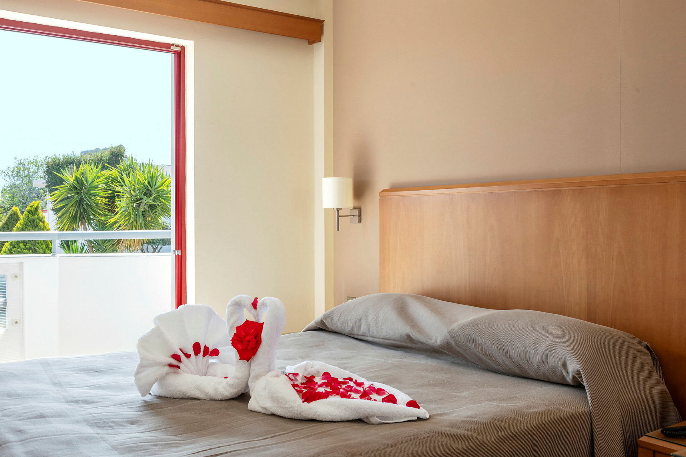 Billede af en seng på et hotelværelse med håndklæder foldet som svaner dekoreret med røde rosenblade. (AI-genereret tekst)