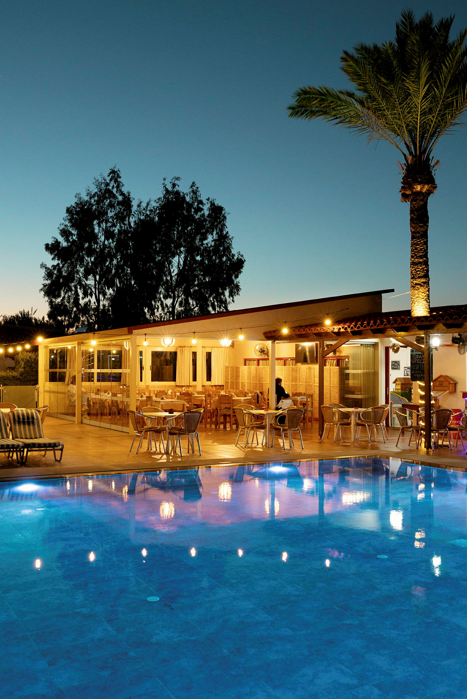 En oplyst restaurant ved en udendørs pool om aftenen. (AI-genereret tekst)