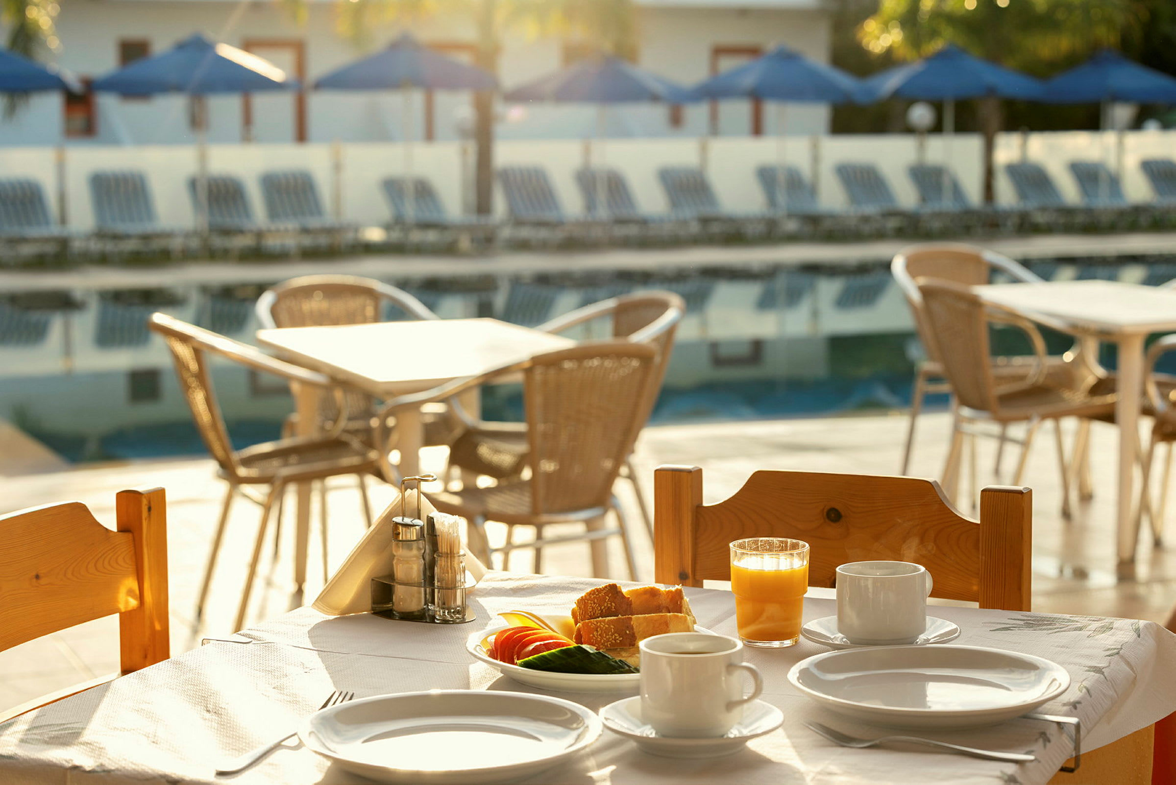 Et morgenbord ved en swimmingpool med service, juice og grøntsager. (AI-genereret tekst)