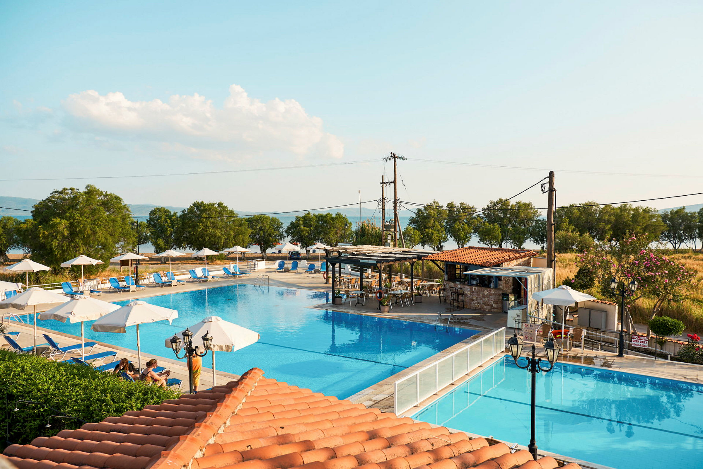 Udendørs swimmingpool med liggestole og parasoller ved strandnært område. (AI-genereret tekst)