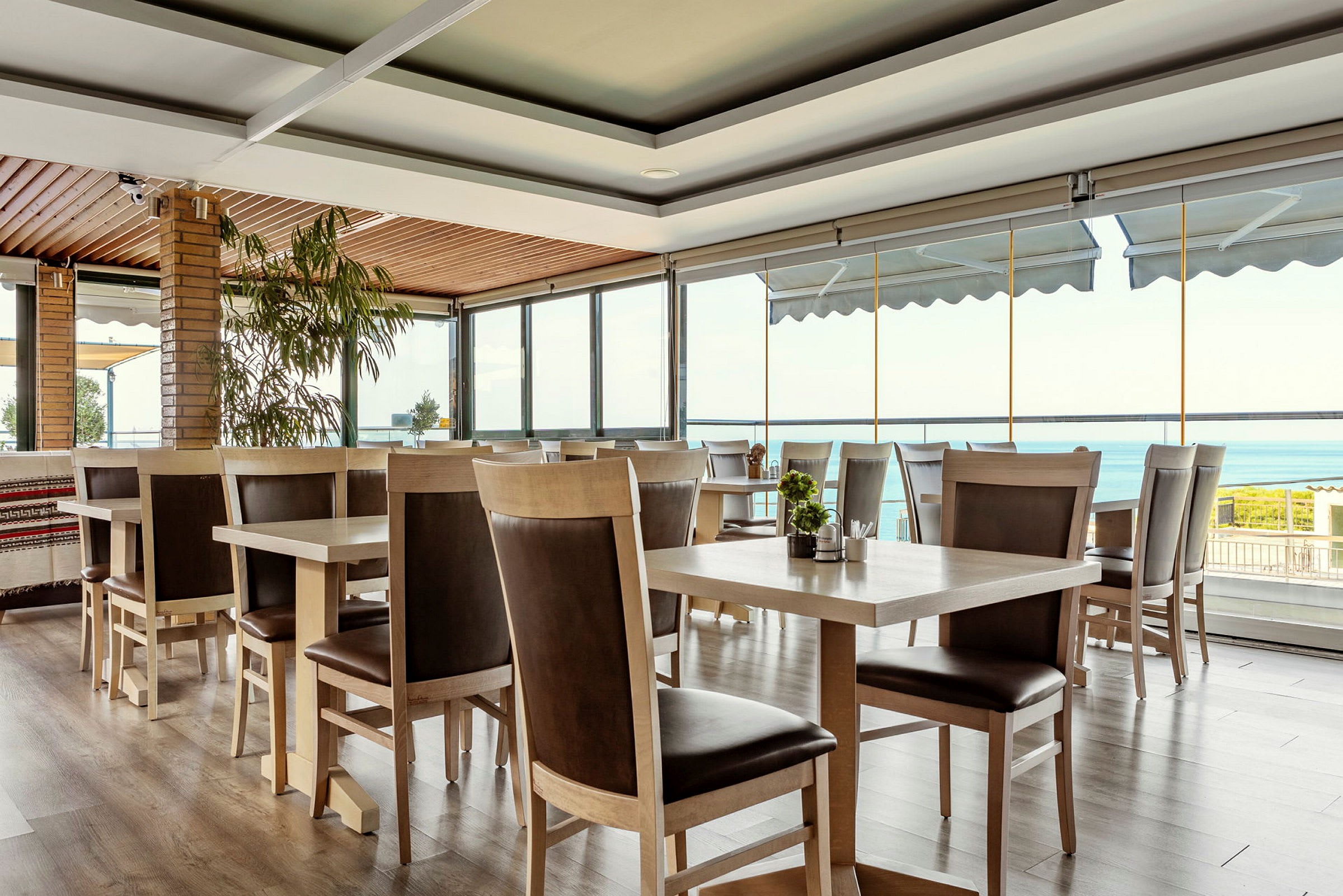 Interiør af en restaurant med træborde og stole, store vinduer med udsigt over havet. (AI-genereret tekst)