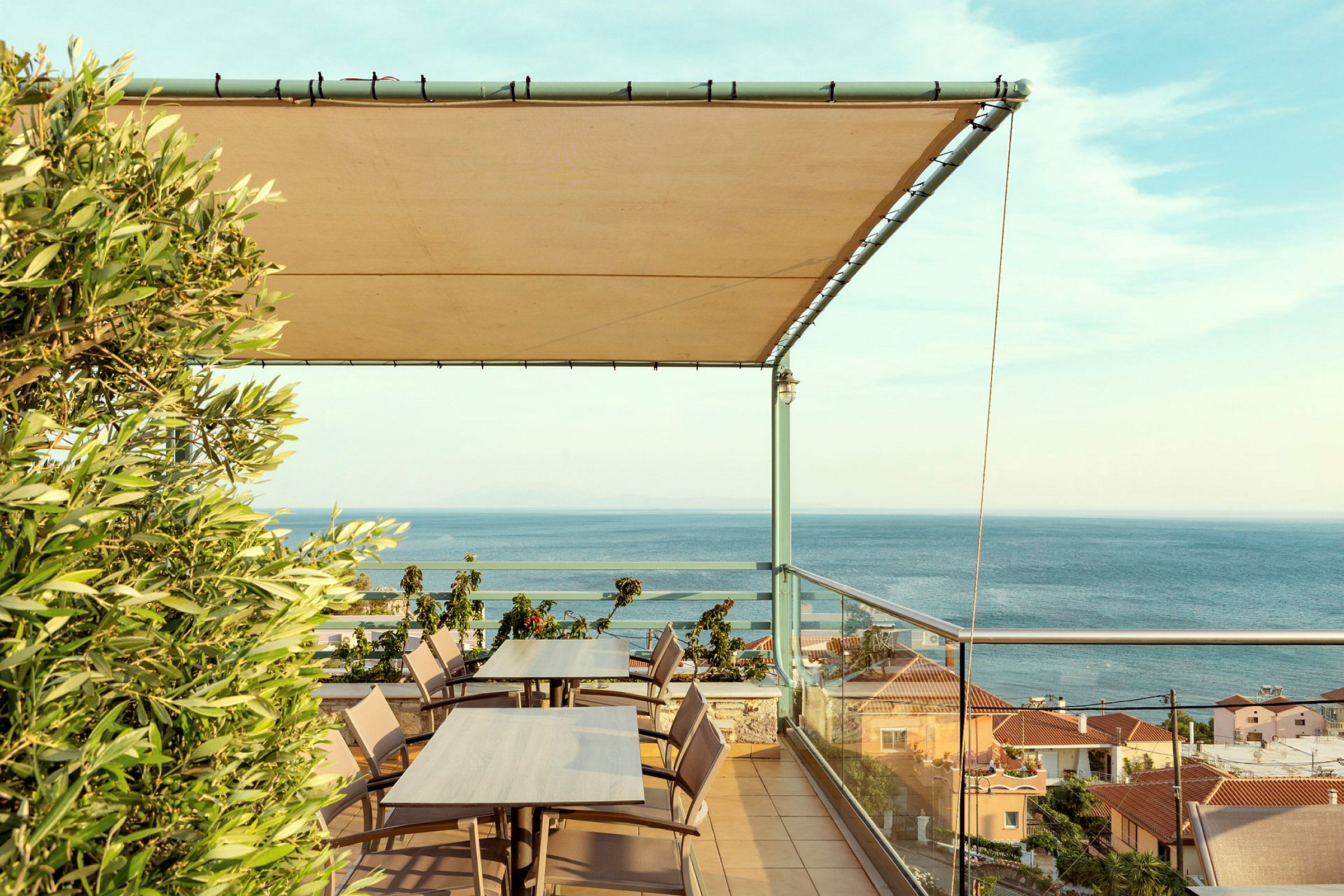 Terrasse med borde og stole, et tag af stof og udsigt over havet og huse. (AI-genereret tekst)