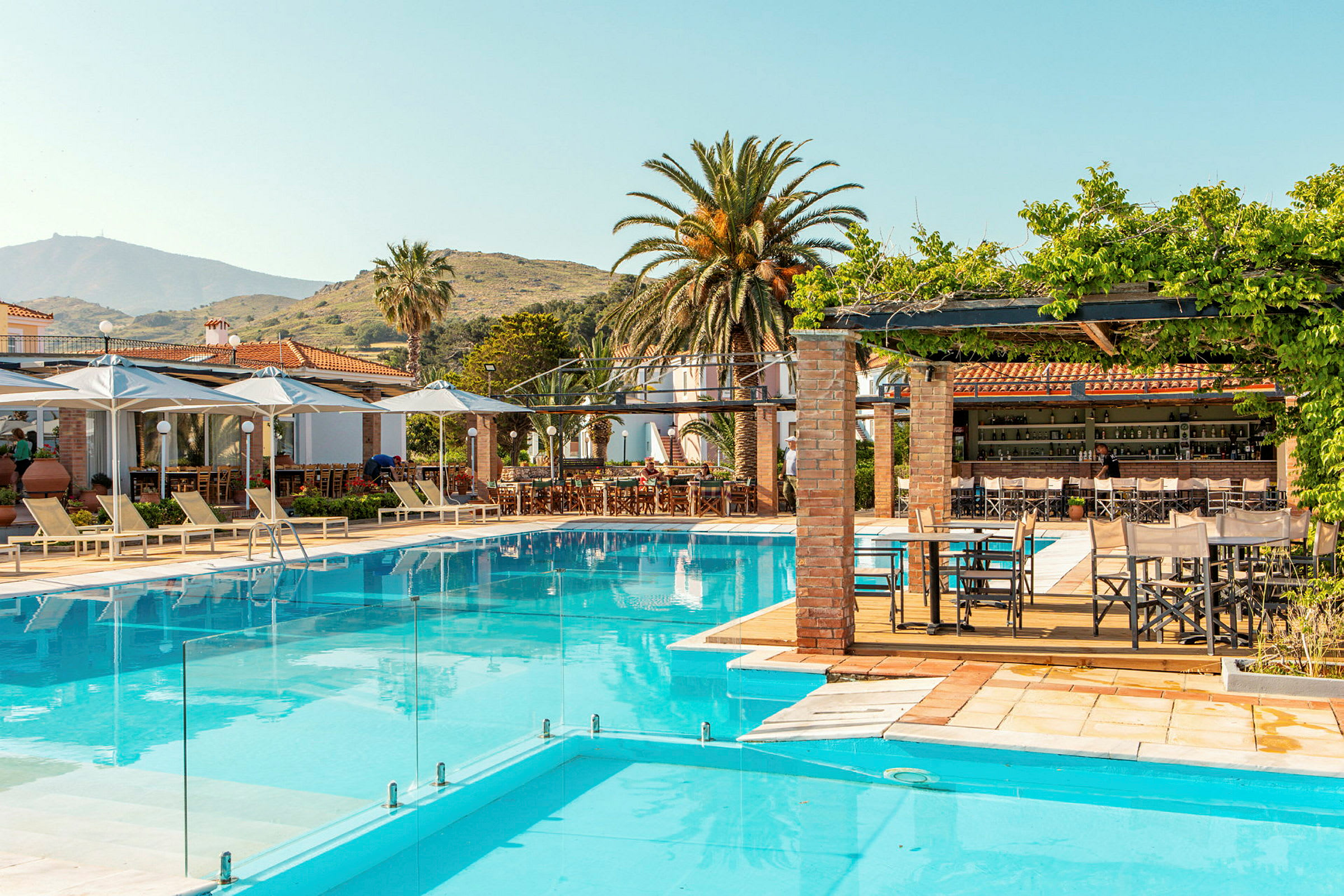 Udendørs swimmingpool med liggestole og nærliggende restaurantområde under parasoller. (AI-genereret tekst)