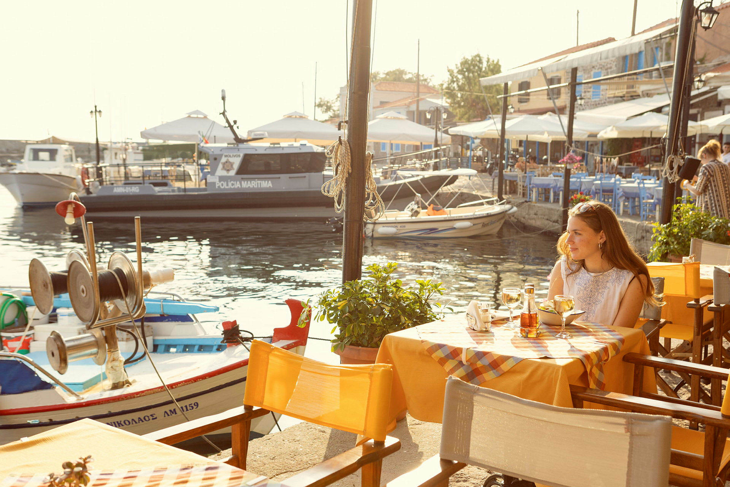 En udendørs restaurant med udsigt over en marina med småbåde og en politibåd. (AI-genereret tekst)