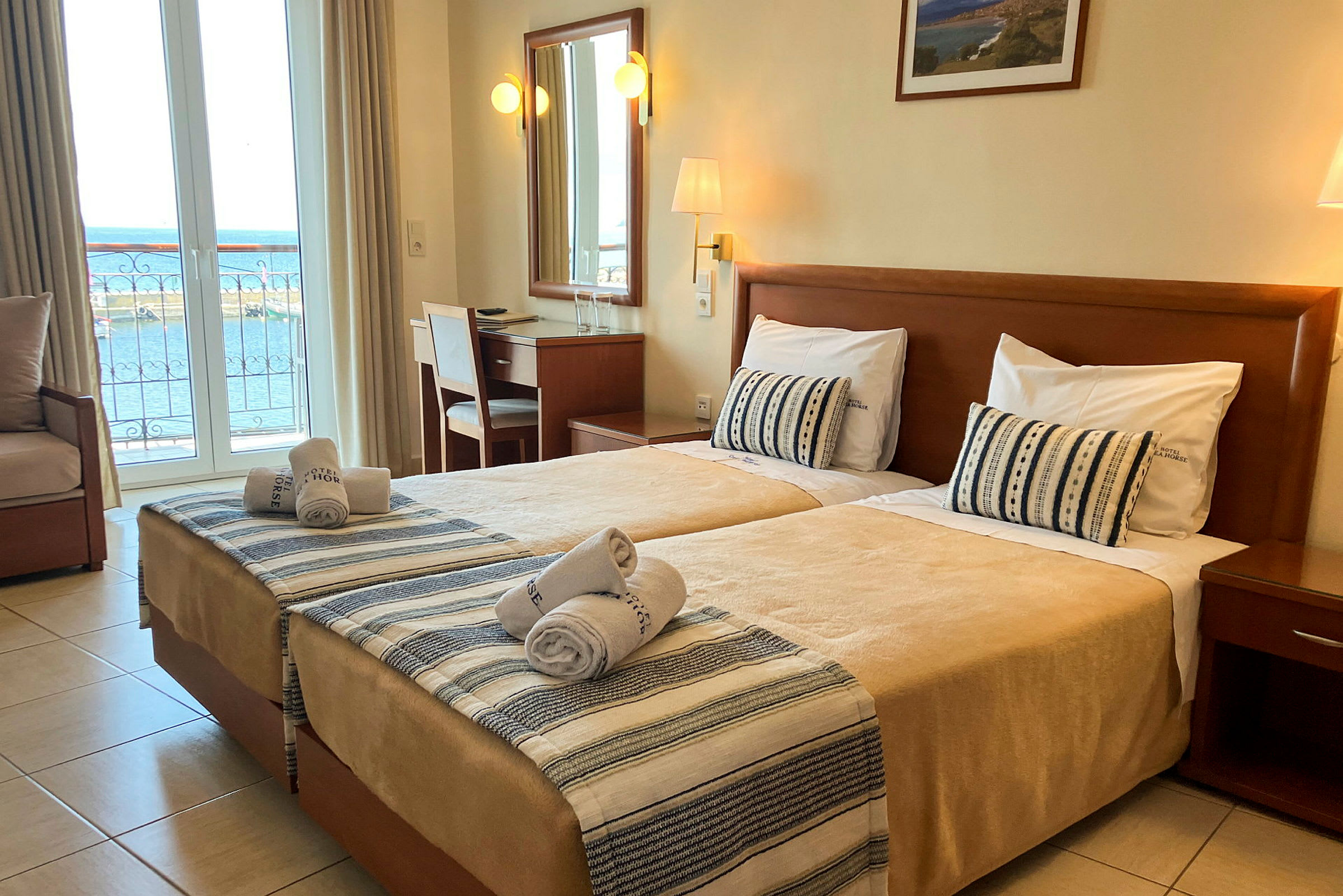 Hotelværelse med to enkeltsenge, skrivebord og udsigt over havet fra altanen. (AI-genereret tekst)