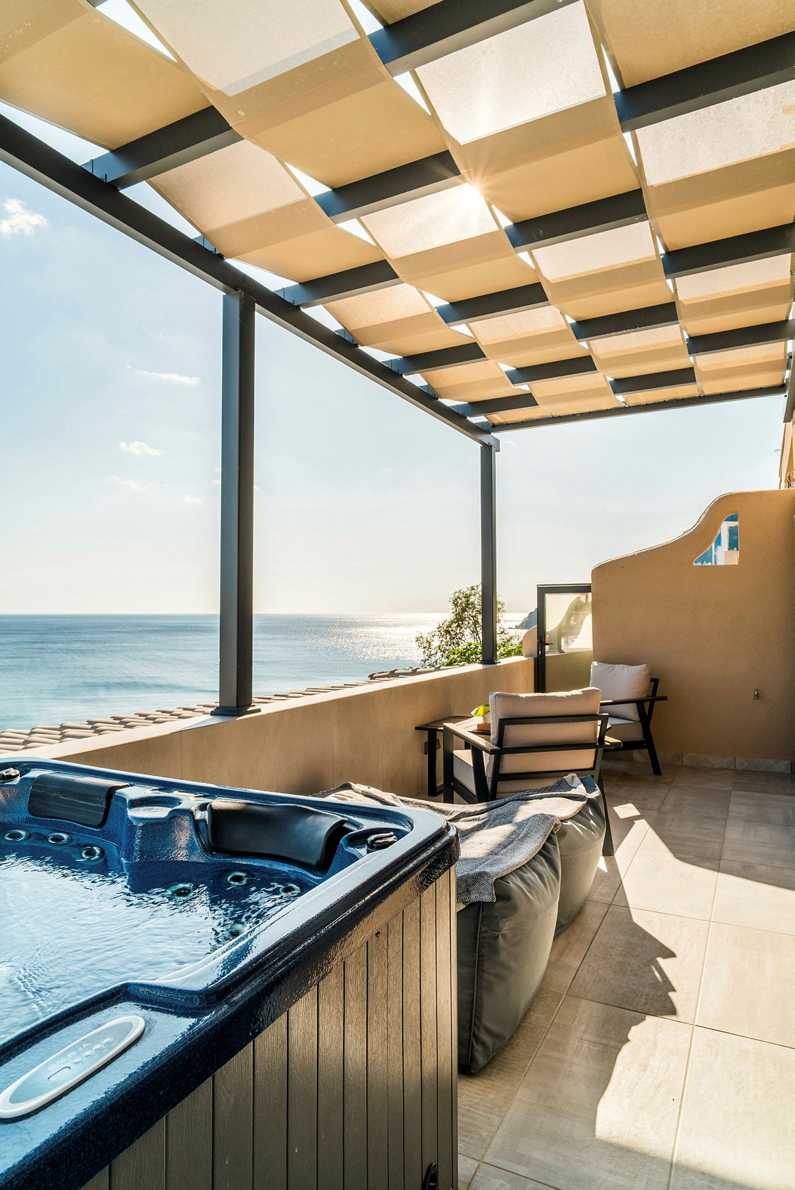 En terrasse med jacuzzi, siddepladser og udsigt over havet under en tagpergola. (AI-genereret tekst)