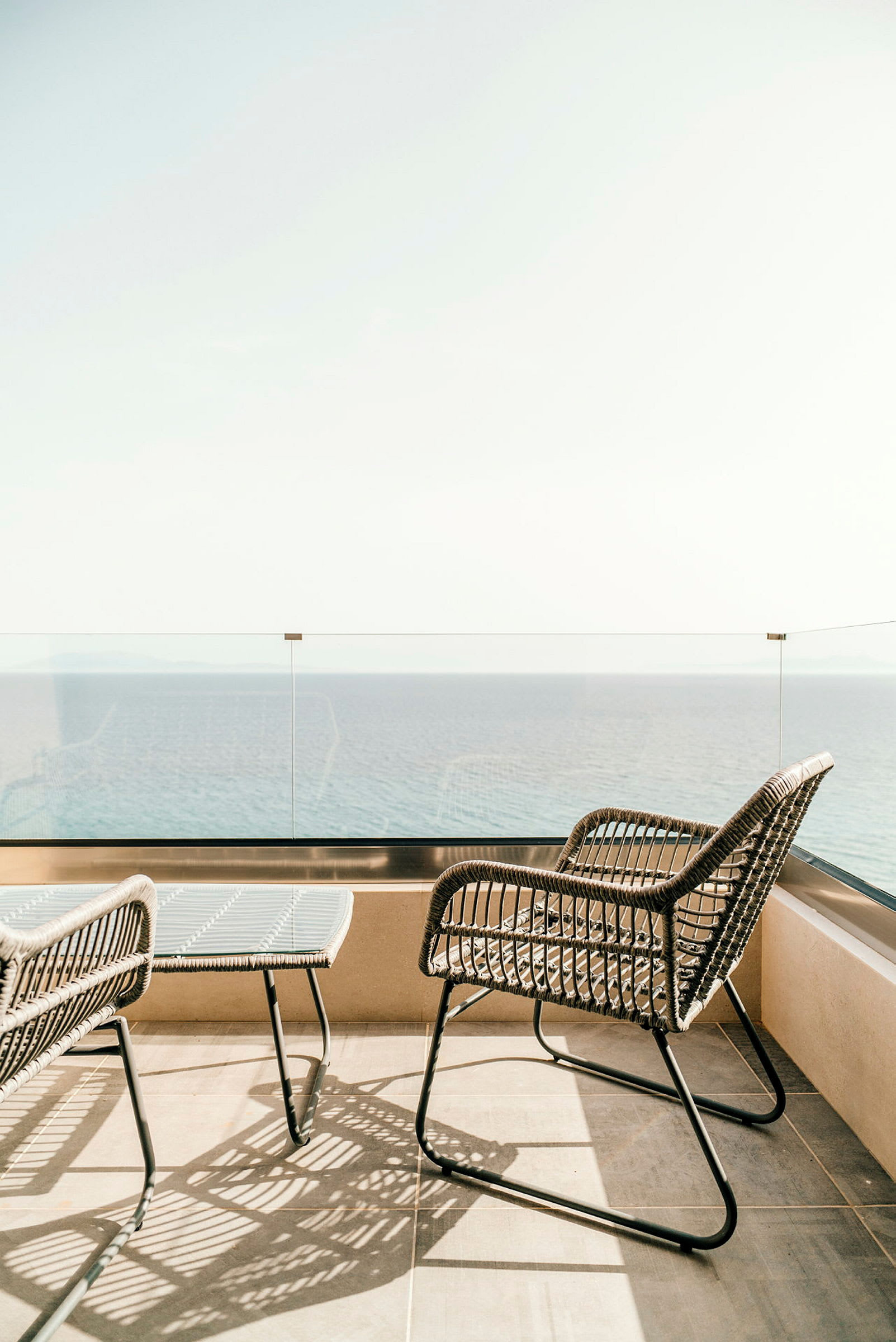 To rottingstole og et lille bord på en balkon med udsigt over havet. (AI-genereret tekst)