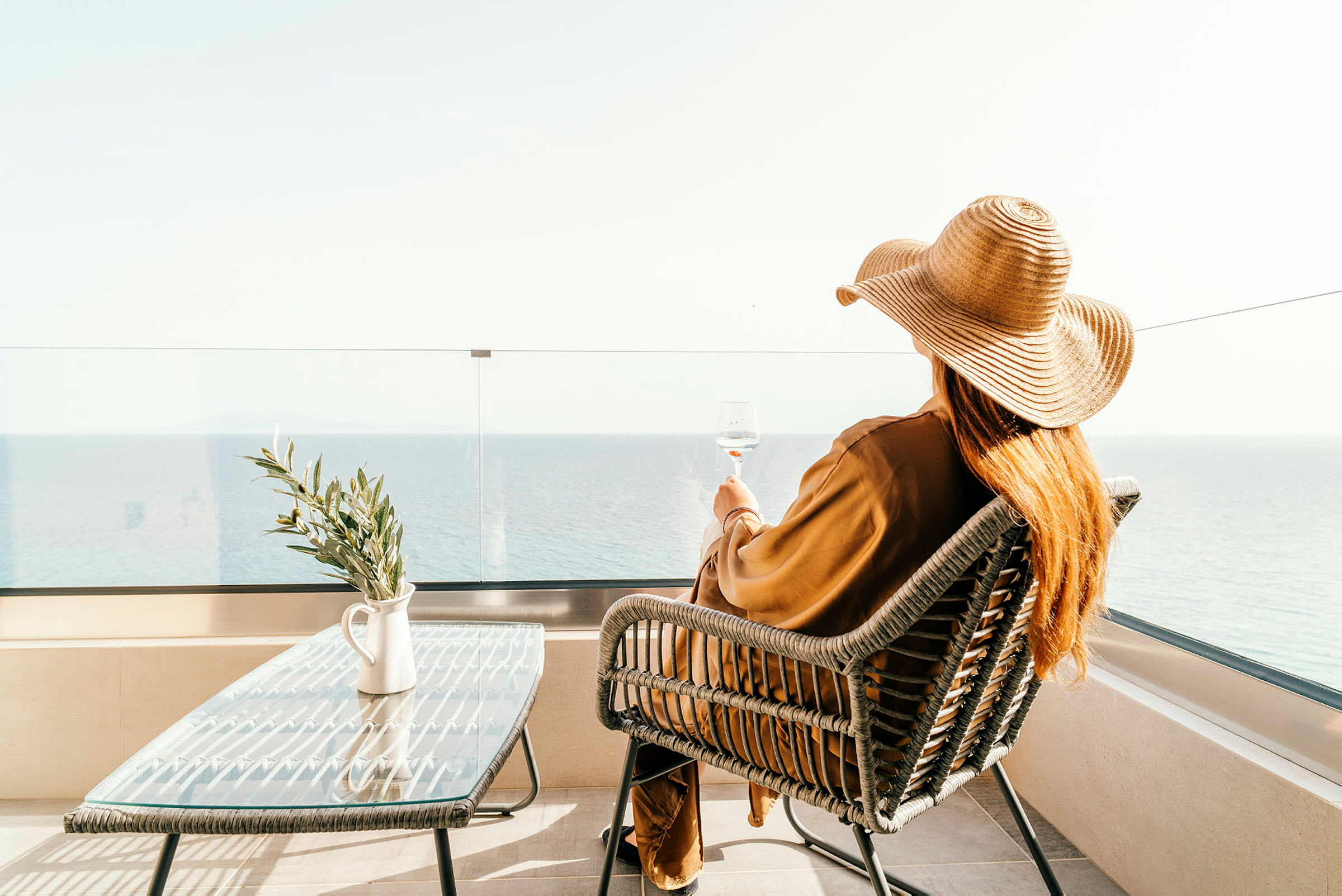 En person med solhat sidder på en terrasse ved havet. (AI-genereret tekst)