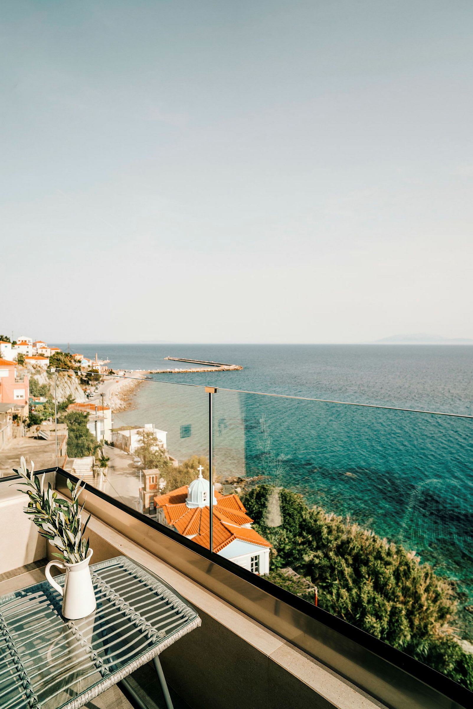 Udsigt over havet fra en balkon med et bord og en vase. (AI-genereret tekst)