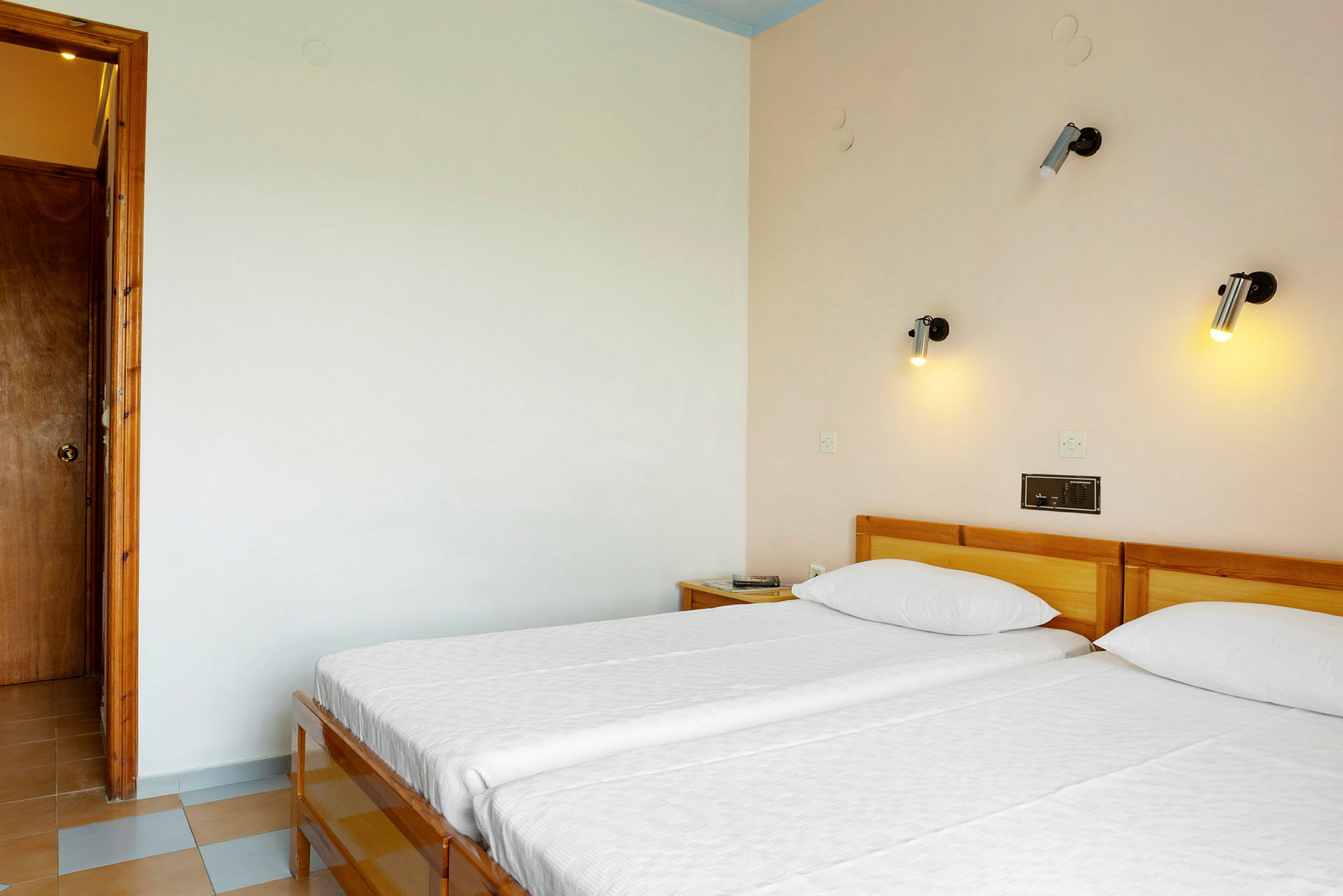 Hotelværelse med to enkeltsenge og væglamper over sengene. (AI-genereret tekst)