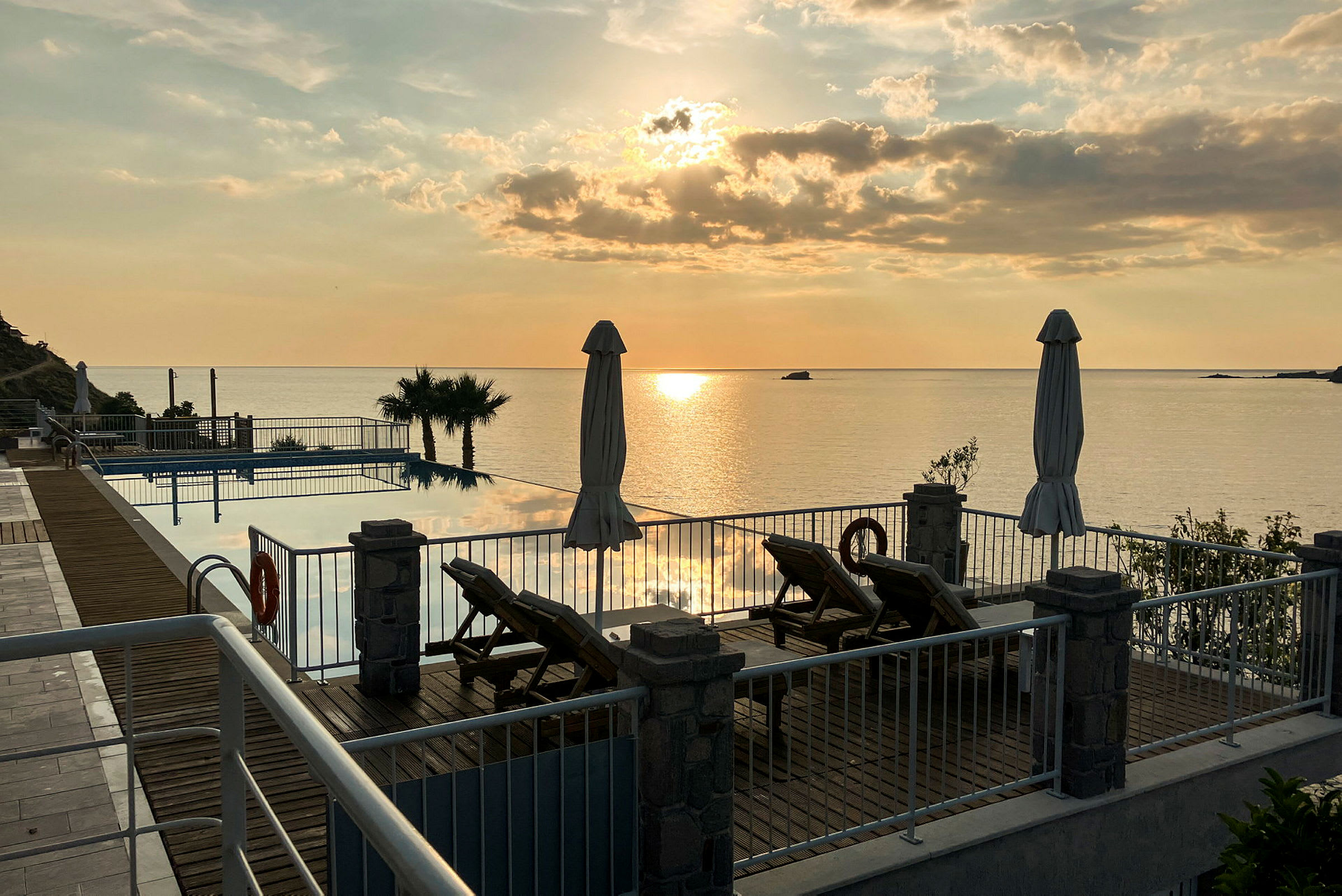 Solnedgang over et poolområde med udsigt til havet. (AI-genereret tekst)