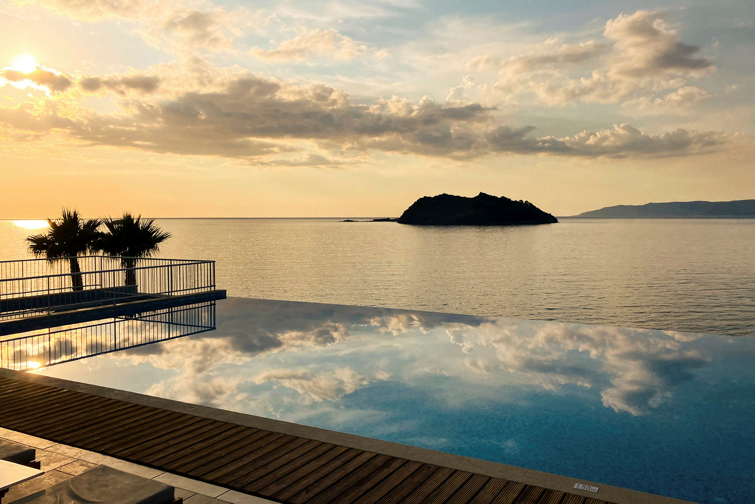 Infinitypool foran en havsolnedgang med en lille ø i baggrunden. (AI-genereret tekst)