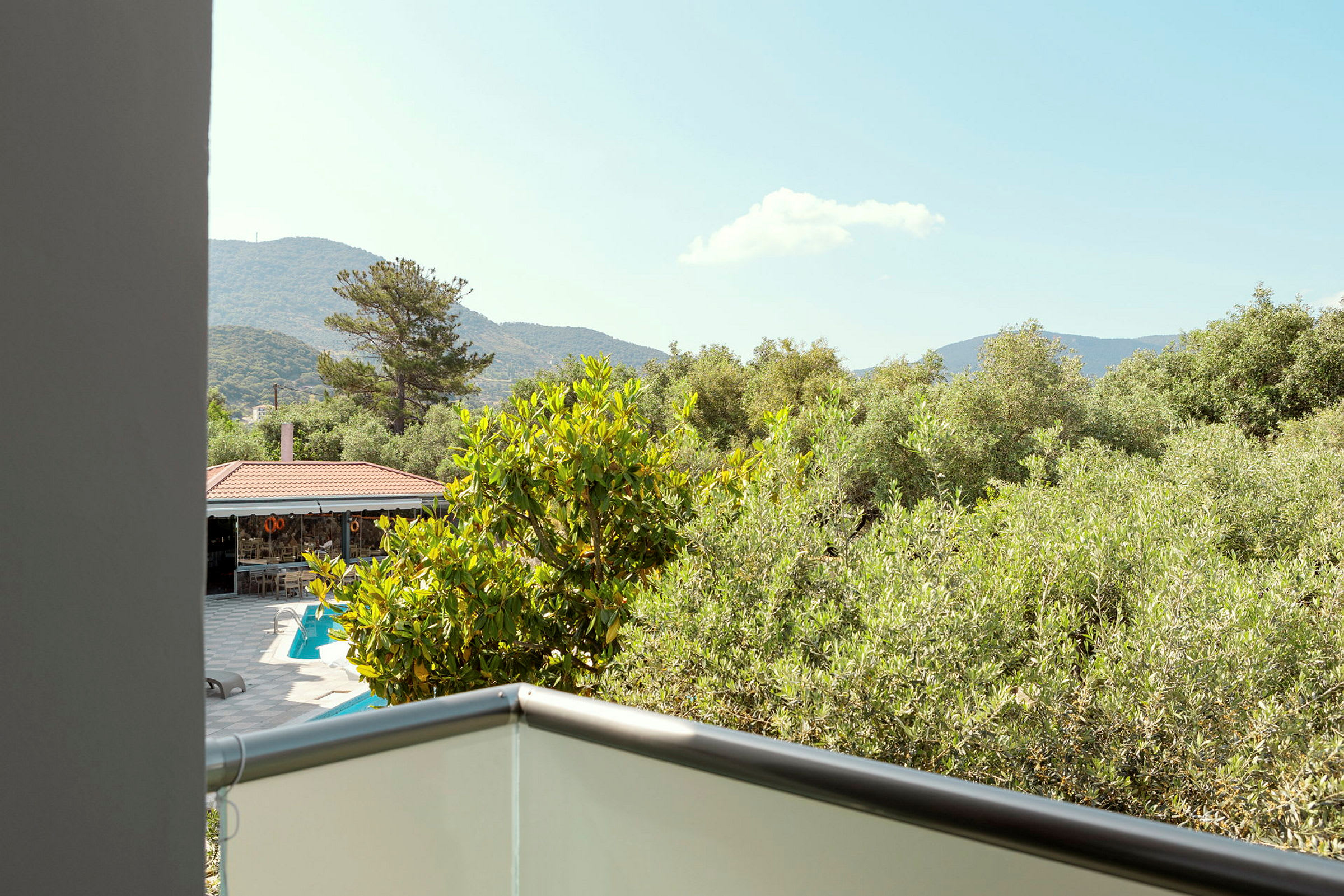 En udsigt fra en balkon, der viser træer, en pool og bjergene i baggrunden. (AI-genereret tekst)