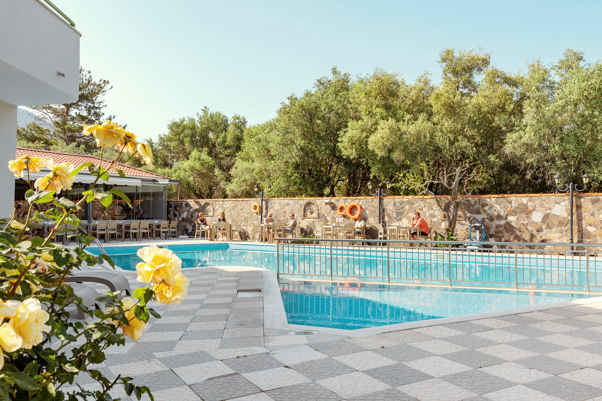Udendørs pool omgivet af stole og borde samt planter og blomster. (AI-genereret tekst)