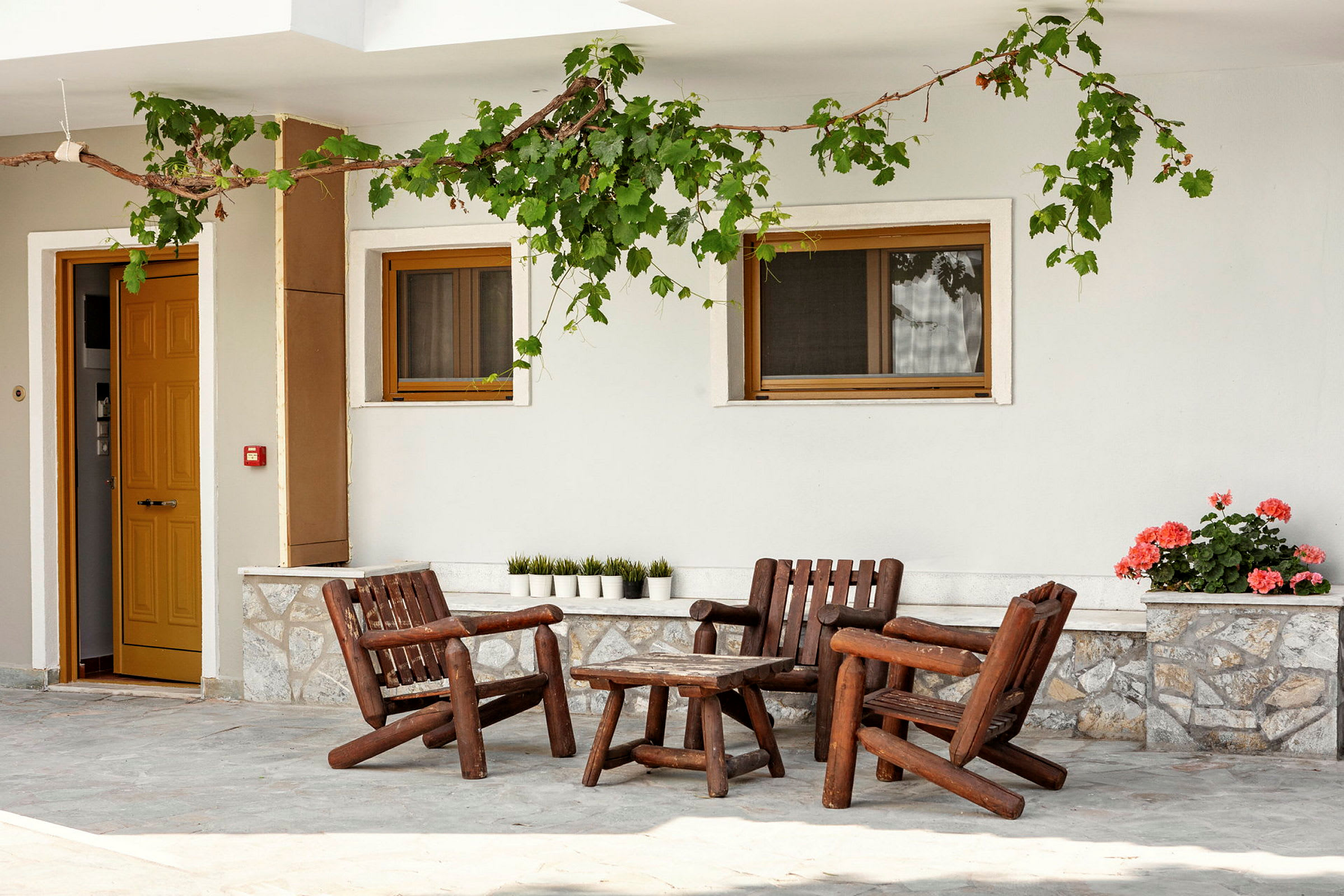 Træmøbler på en terrasse foran en bygning med gul dør og vinduer. (AI-genereret tekst)