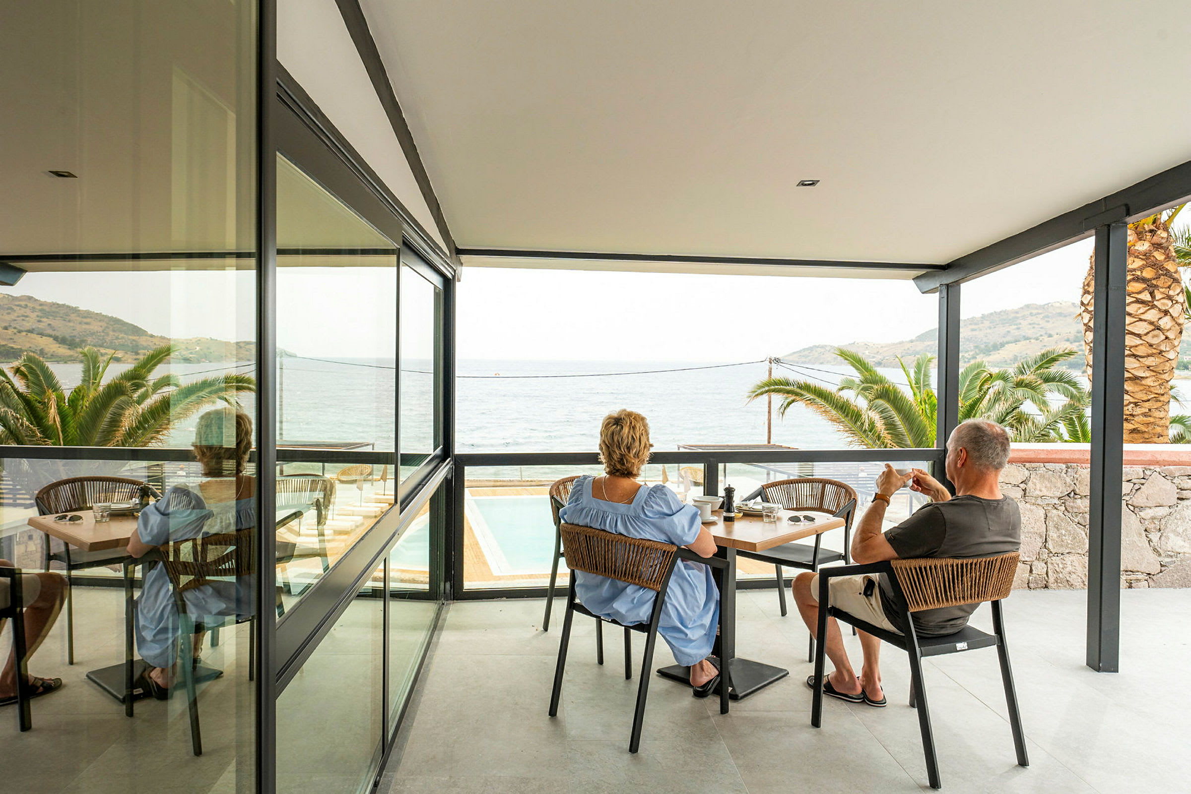 To personer sidder ved et bord på en terrasse med udsigt over havet. (AI-genereret tekst)