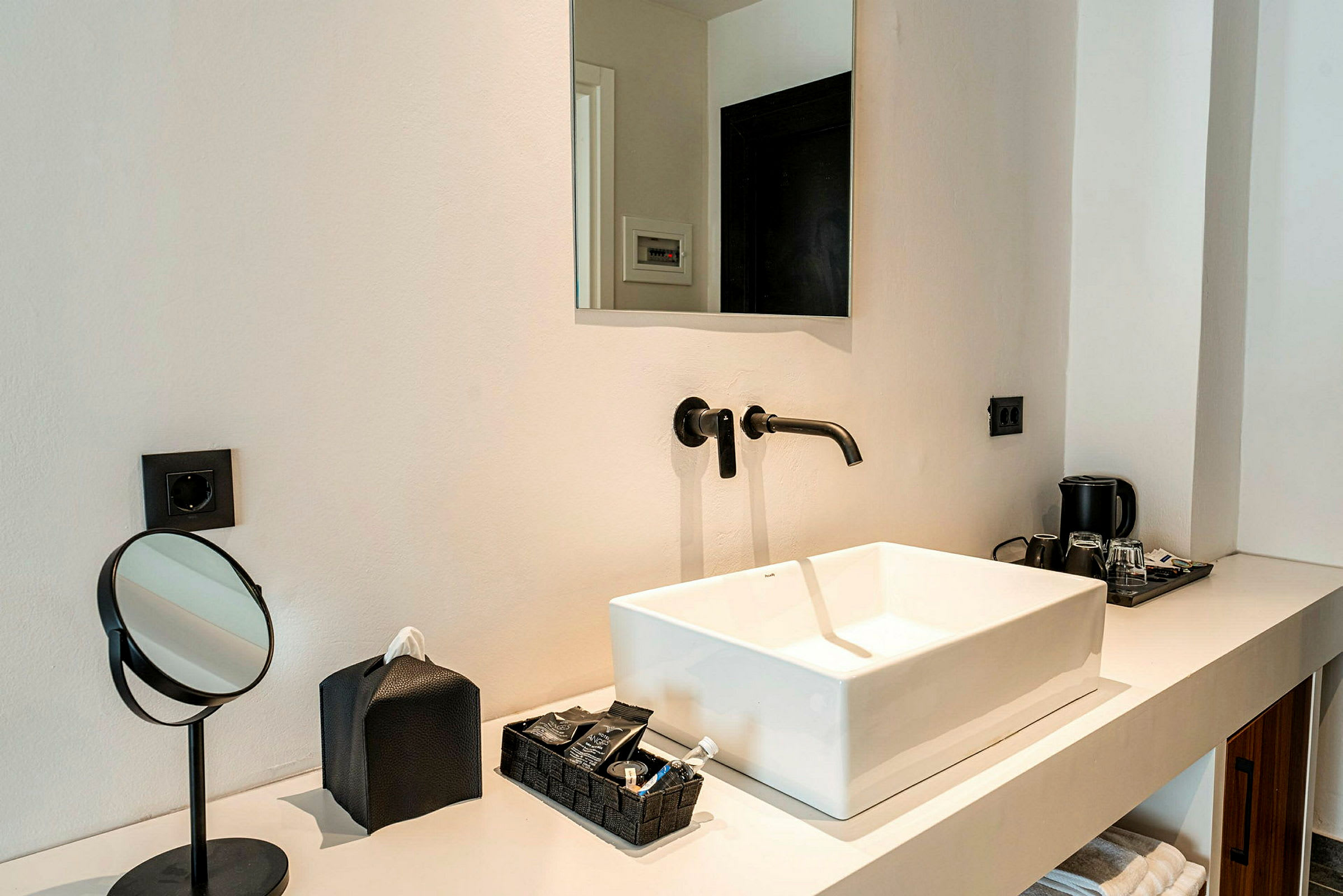 Billede af en moderne håndvask med sort vandhane på en hvid bordplade, komplet med et spejl og toiletartikler. (AI-genereret tekst)