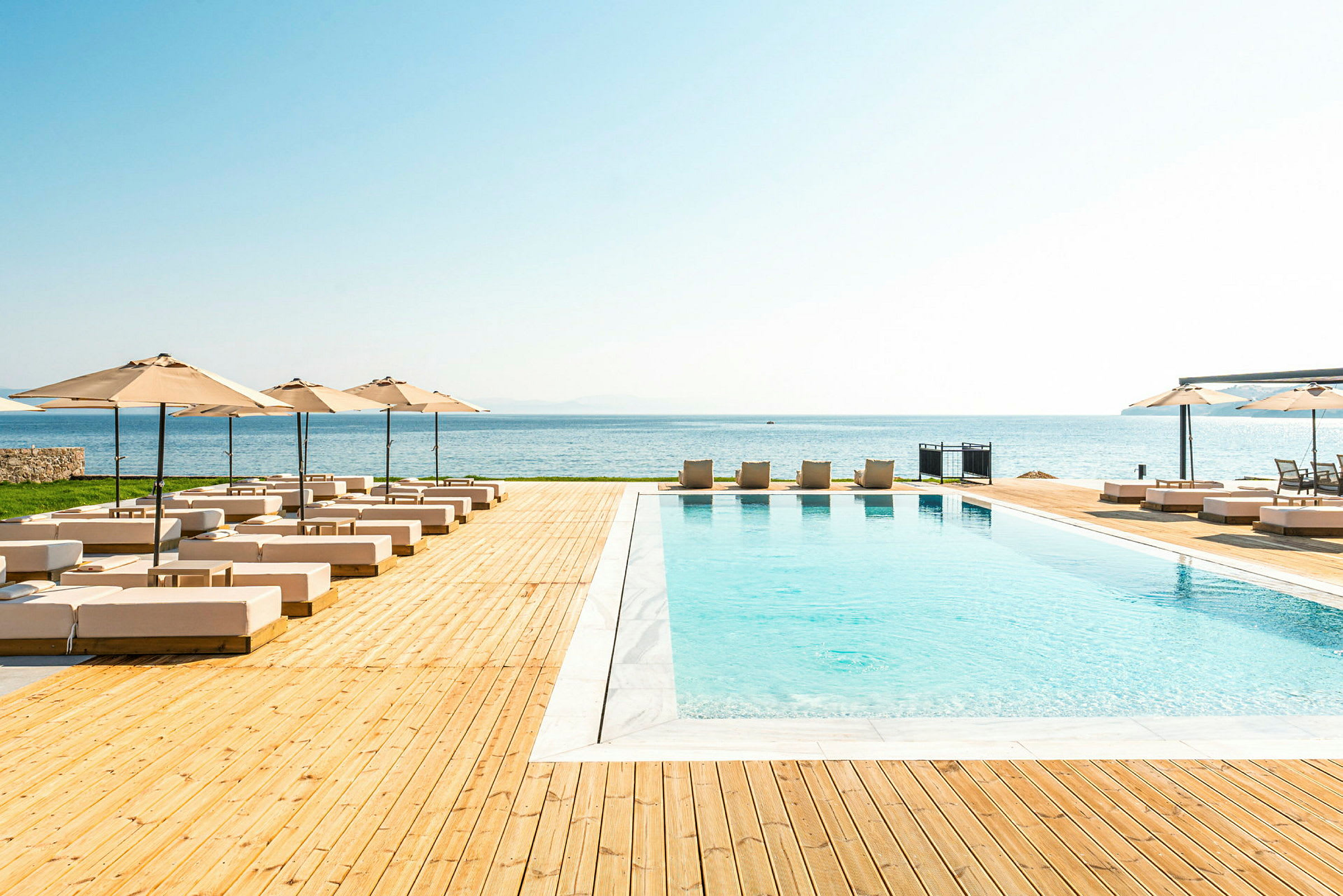 Udendørs pool med liggestole og parasoller ved havet. (AI-genereret tekst)