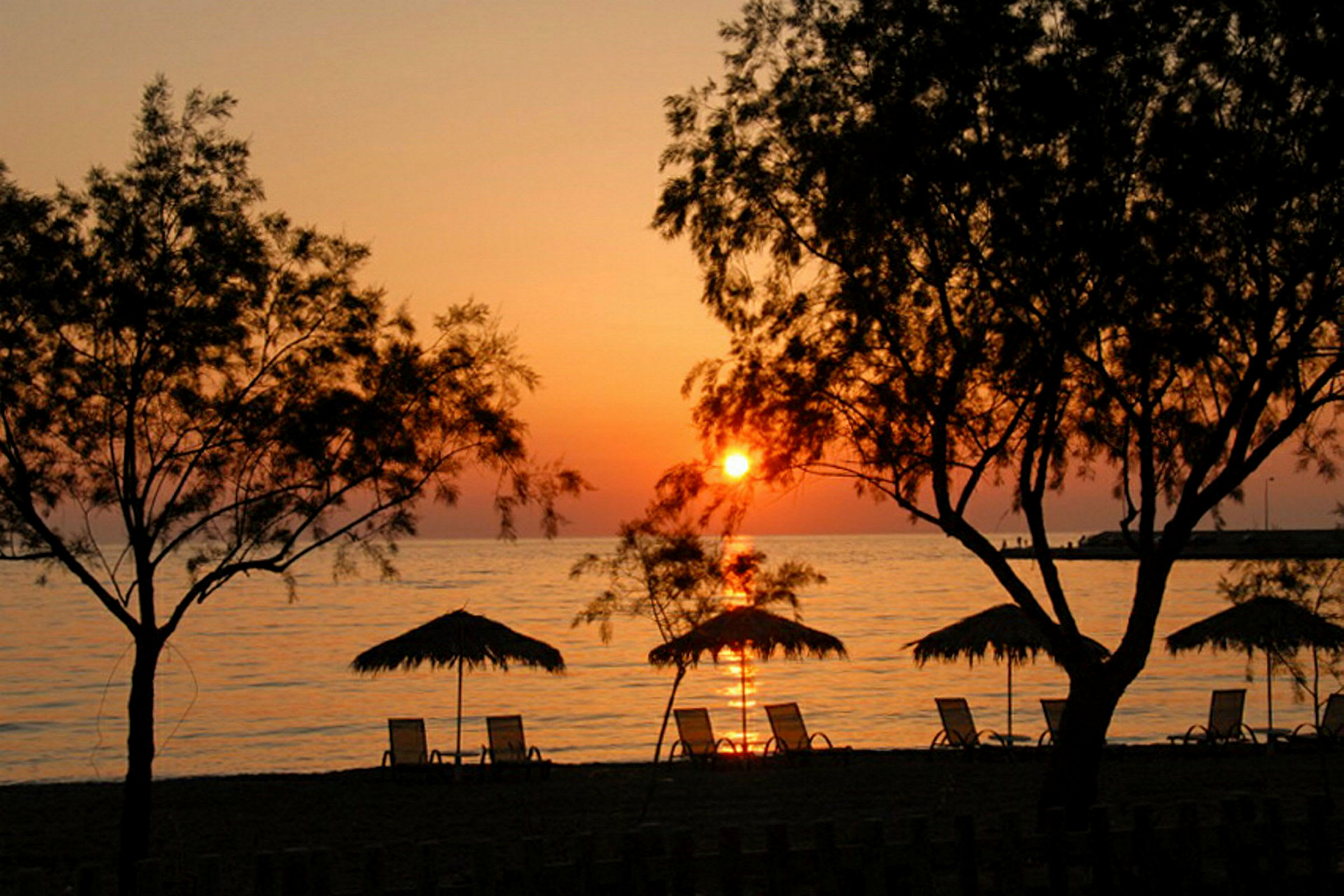 Strand med parasoller og liggestole ved solnedgang. (AI-genereret tekst)