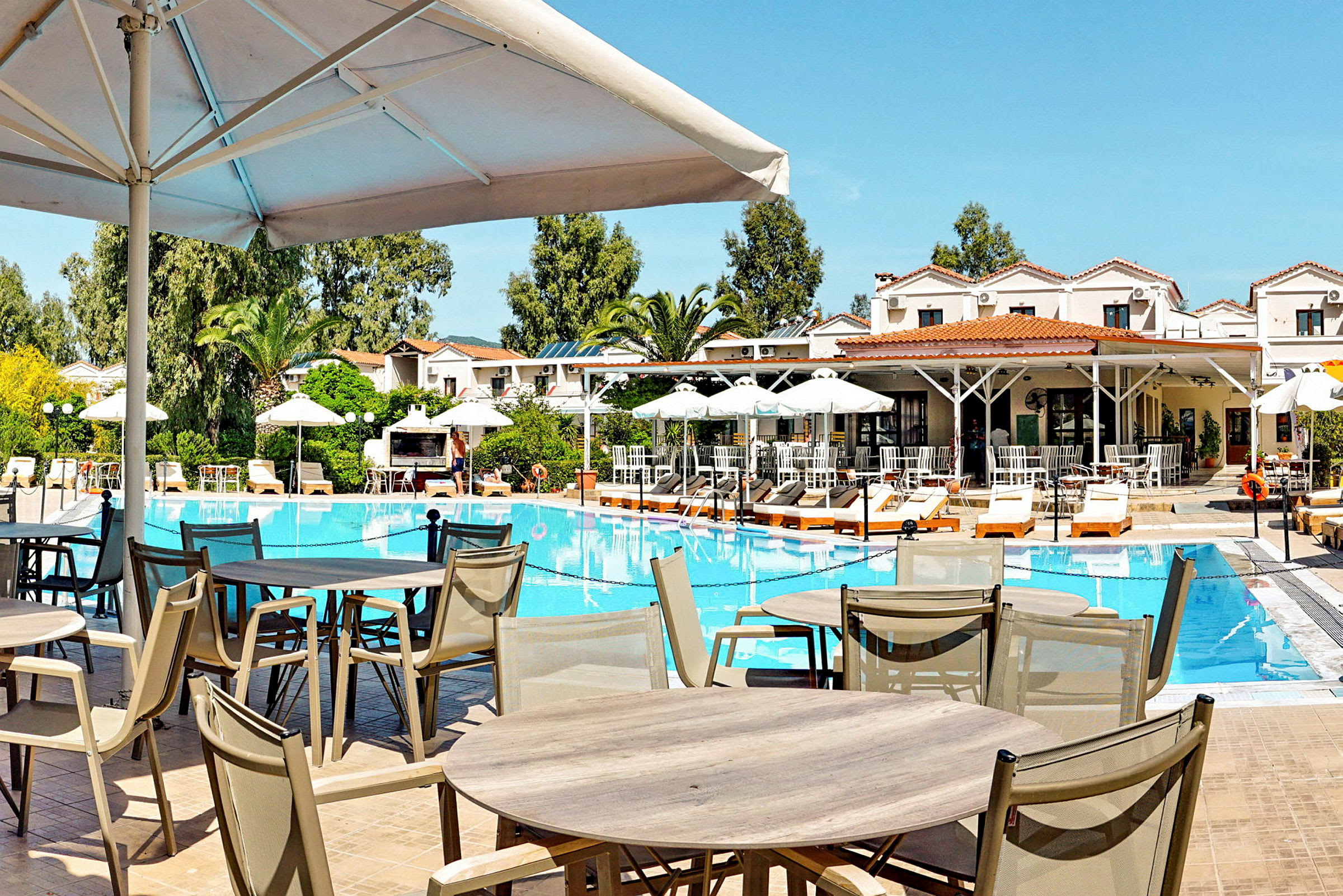 Billede af en udendørs pool omgivet af liggestole og parasoller, med en restaurantbygning i baggrunden. (AI-genereret tekst)