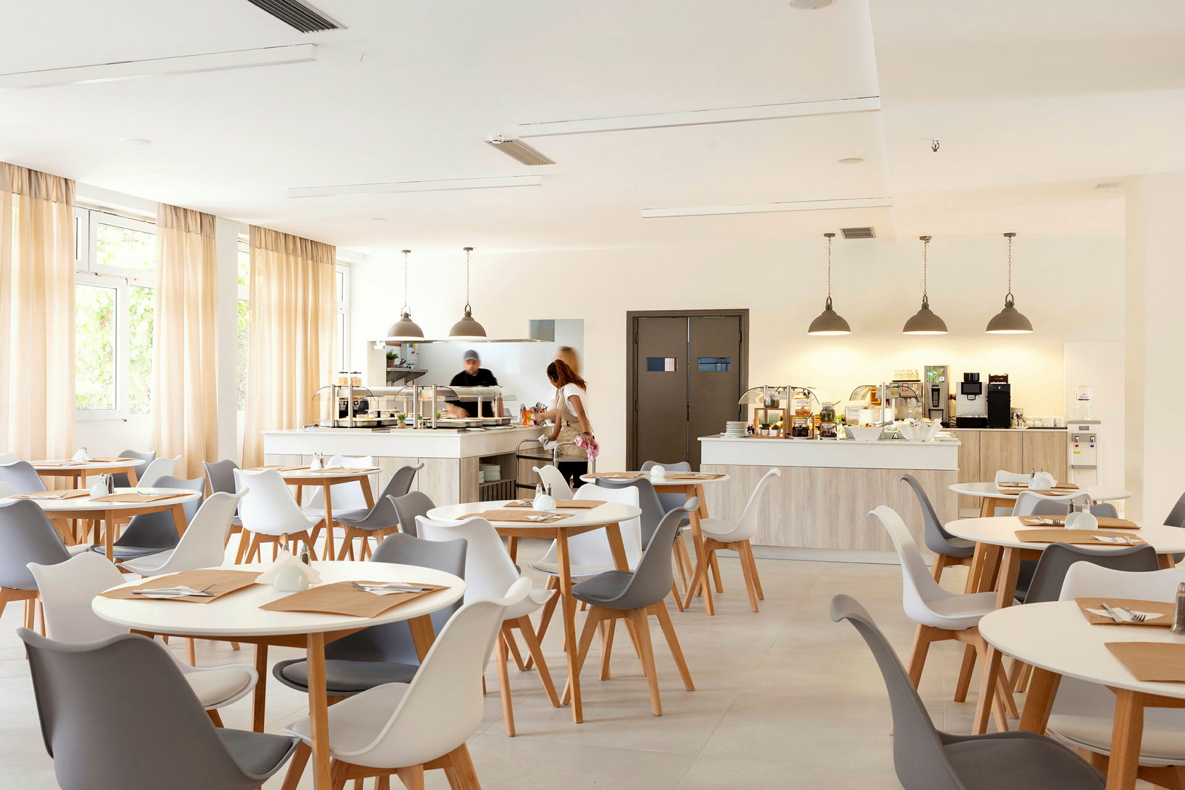 En lys og moderne café med hvide og grå stole samt lys træindretning. (AI-genereret tekst)