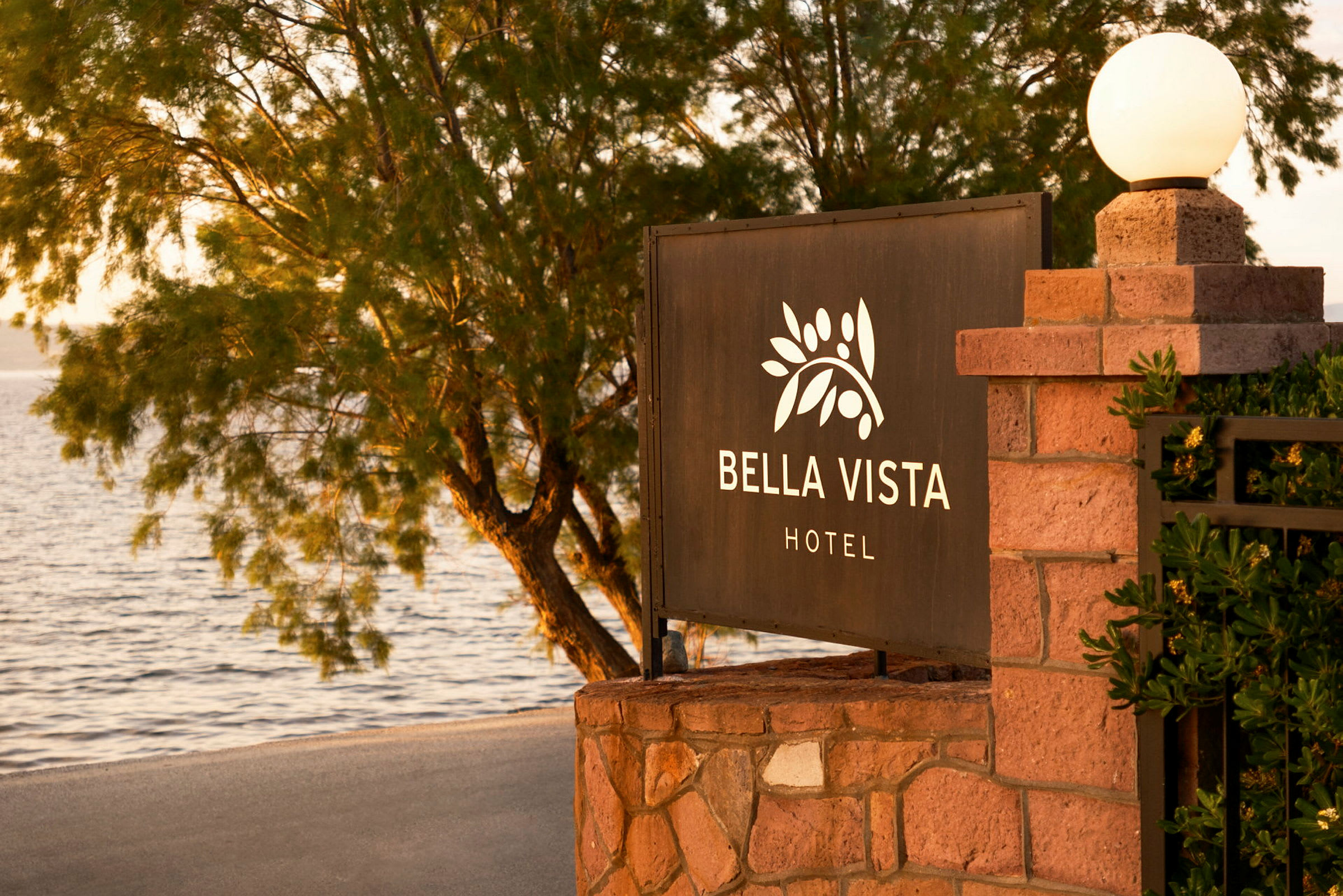 Skilt med teksten "Bella Vista Hotel" ved en strand med træer i baggrunden. (AI-genereret tekst)